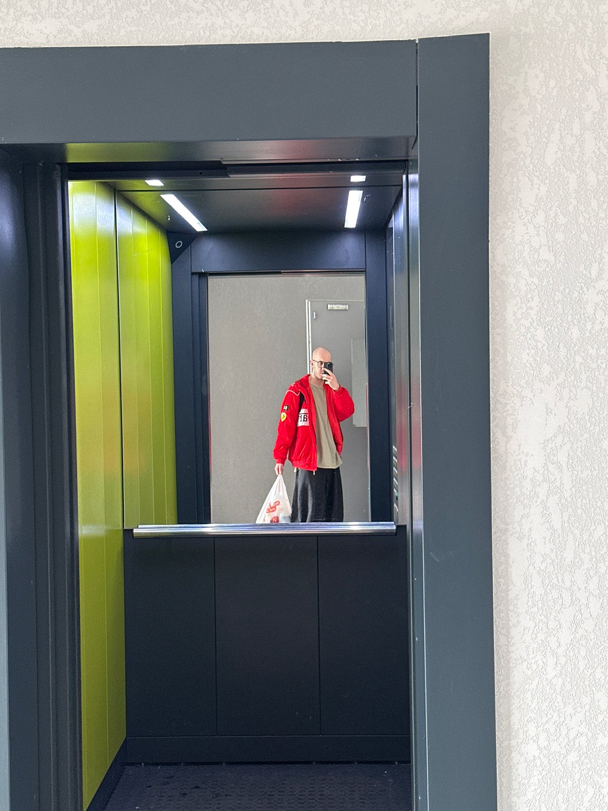 Person in red jacket photographed in elevator mirror