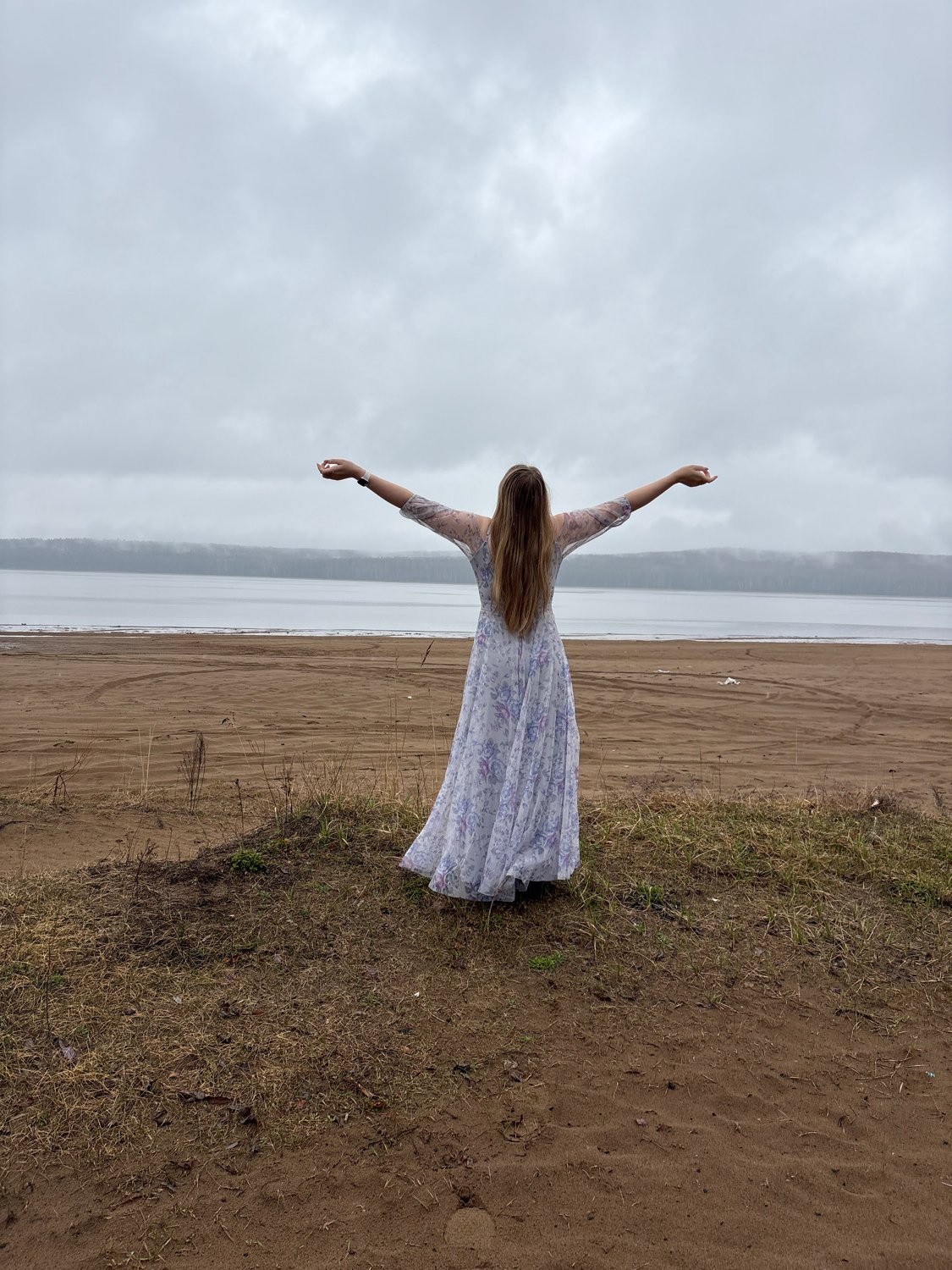 Woman stands on shoreline under cloudy skies in Chaikovsky