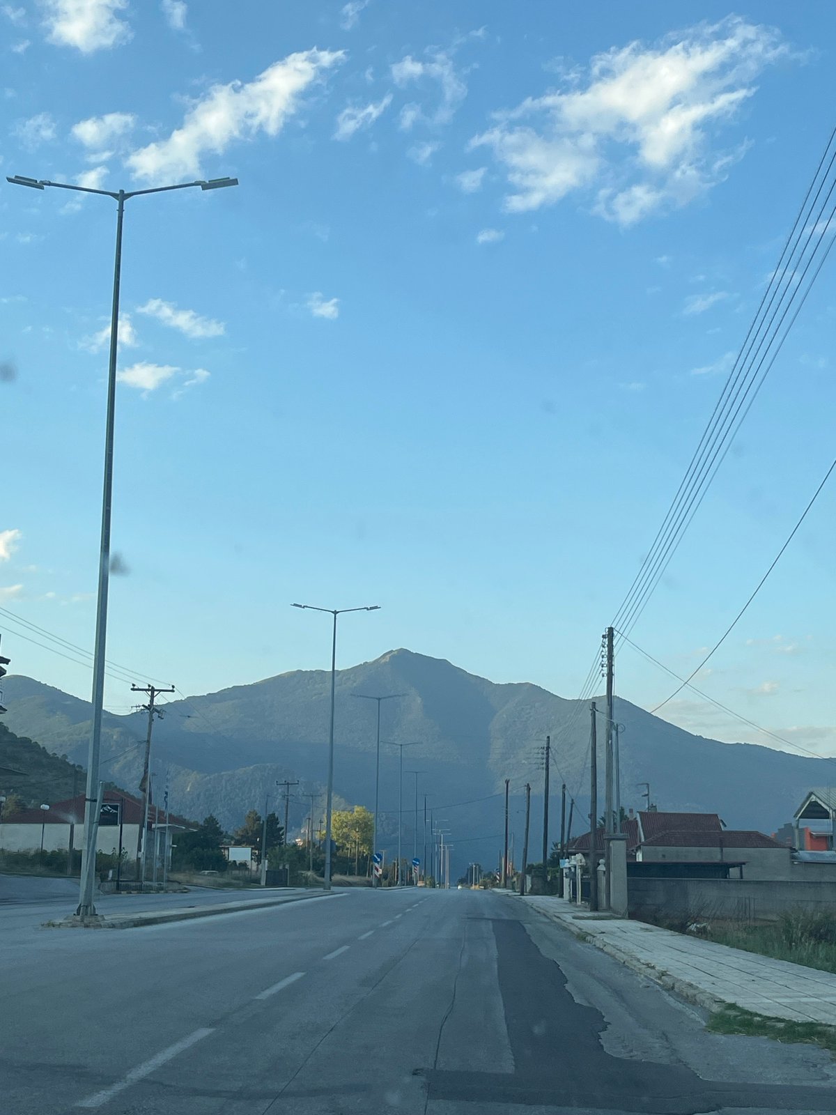 Tree-covered mountain backdrop frames a quiet Greek town road