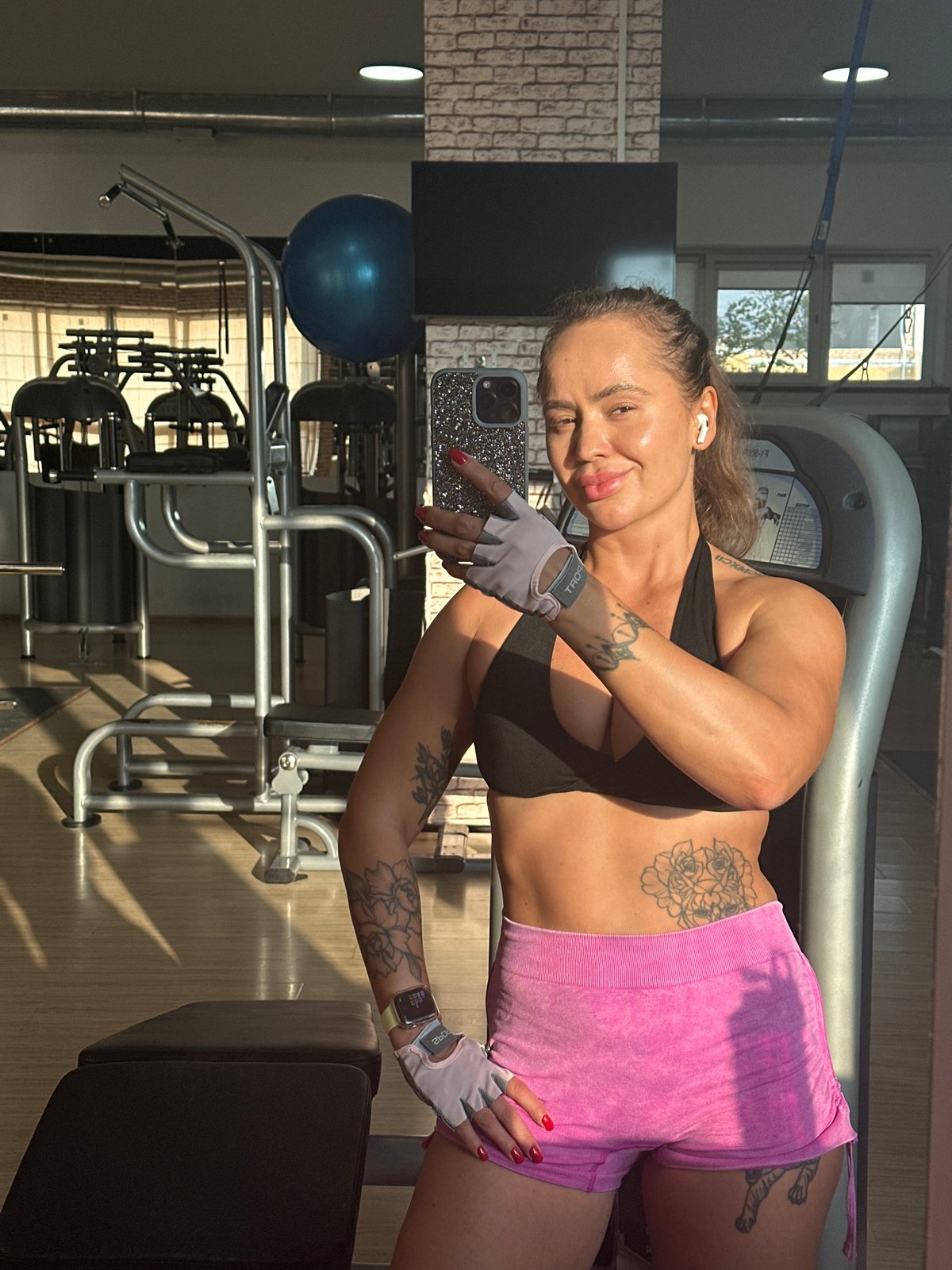 Gym selfie mid-workout, gloves and earbuds on.
