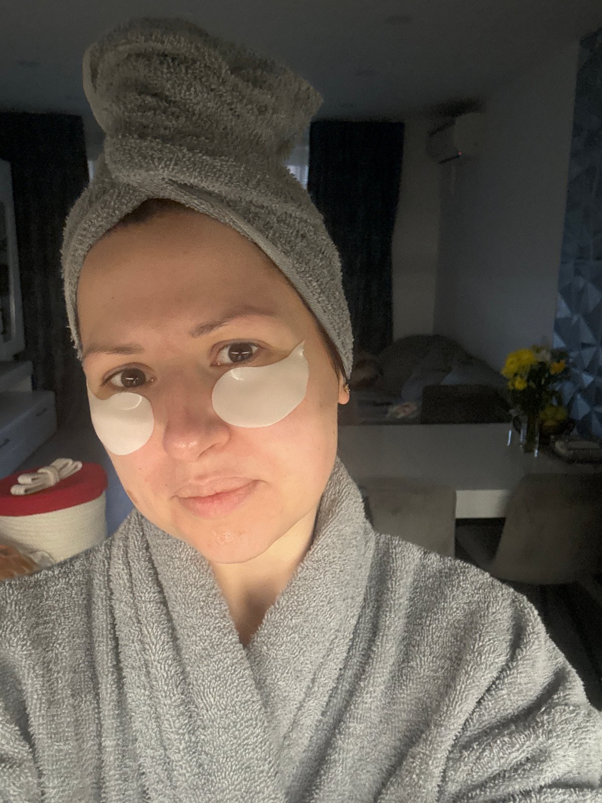 Woman in bathrobe with facial patches holds mug indoors