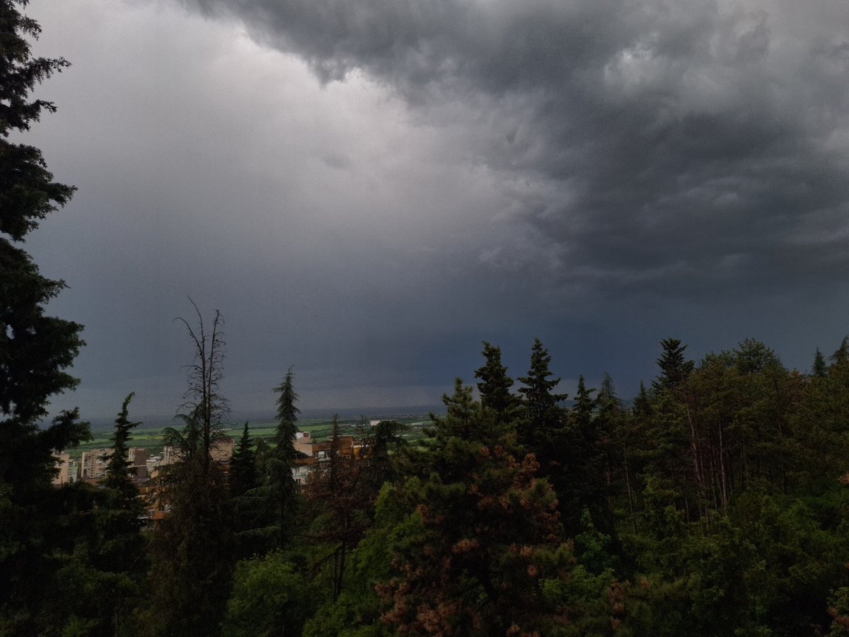 Storm clouds gather over wooded landscape with distant buildings