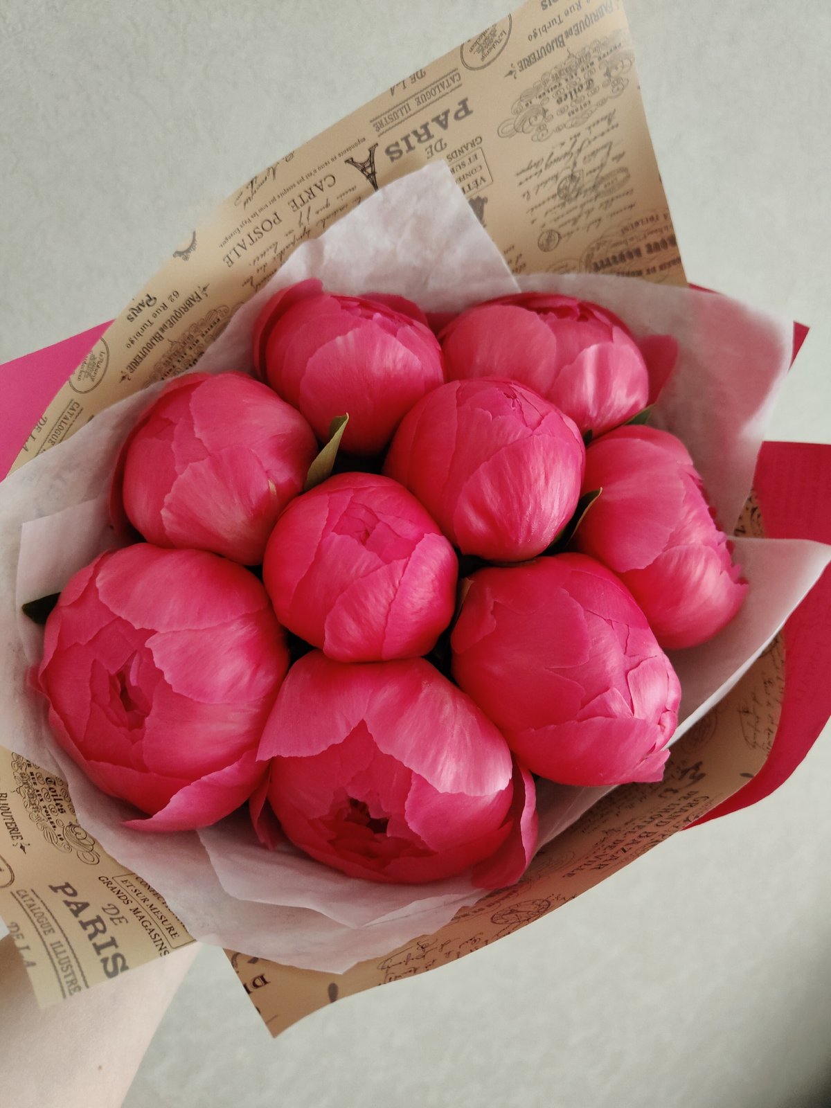 Person holds pink peony bouquet in layered paper wrapping