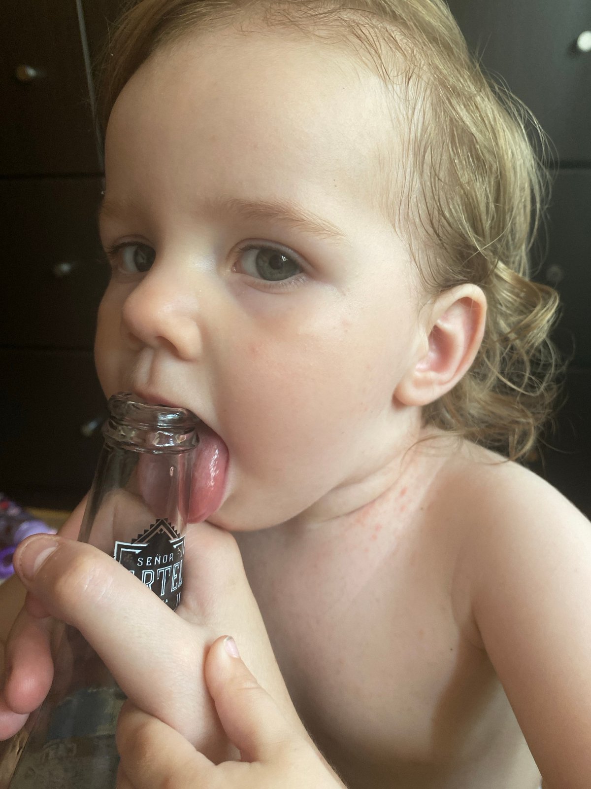Toddler mouths beer bottle rim alongside Cartel beer close-ups