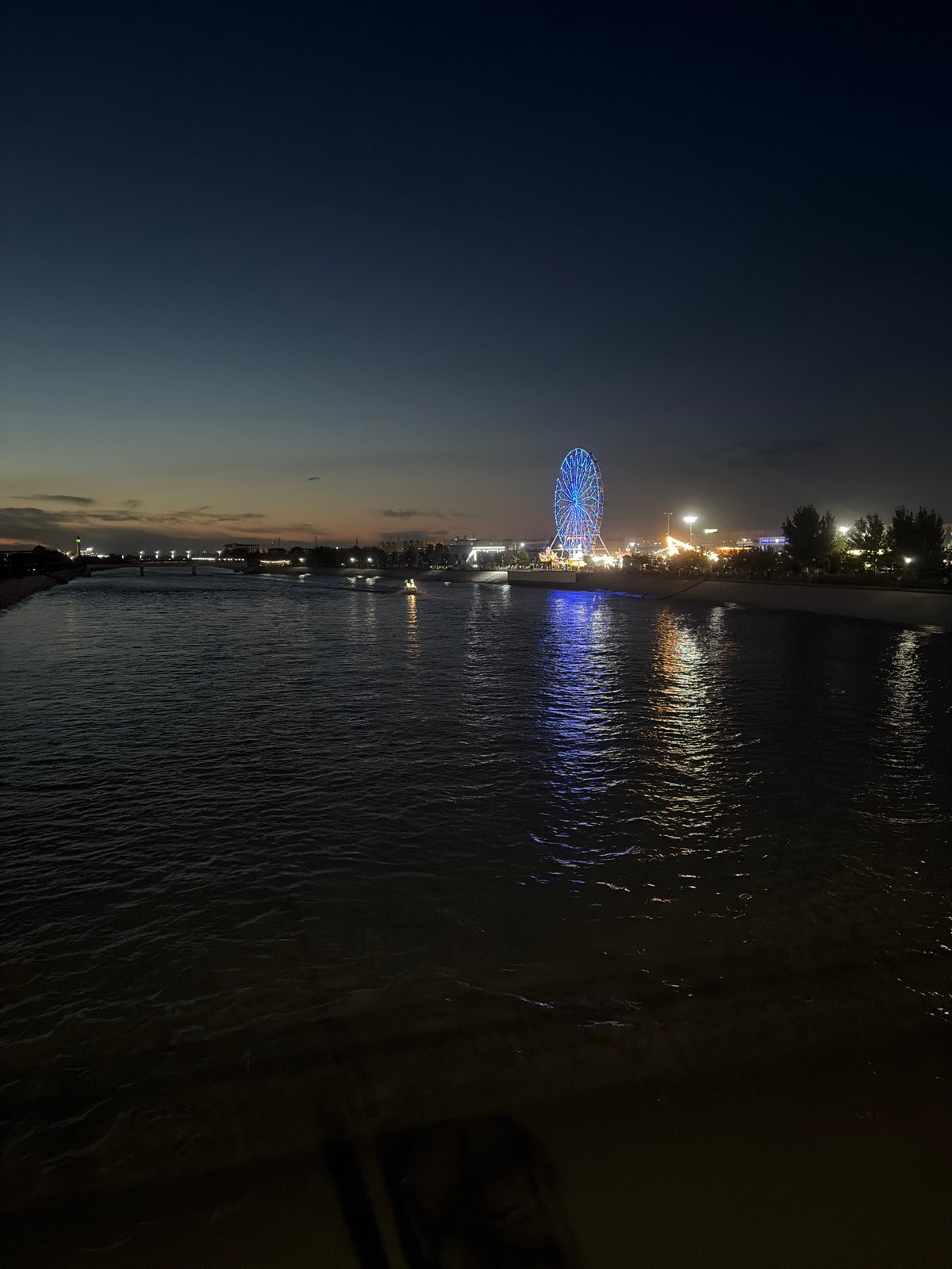 Blue-lit Ferris wheel glows on a Nukus waterfront pier at night