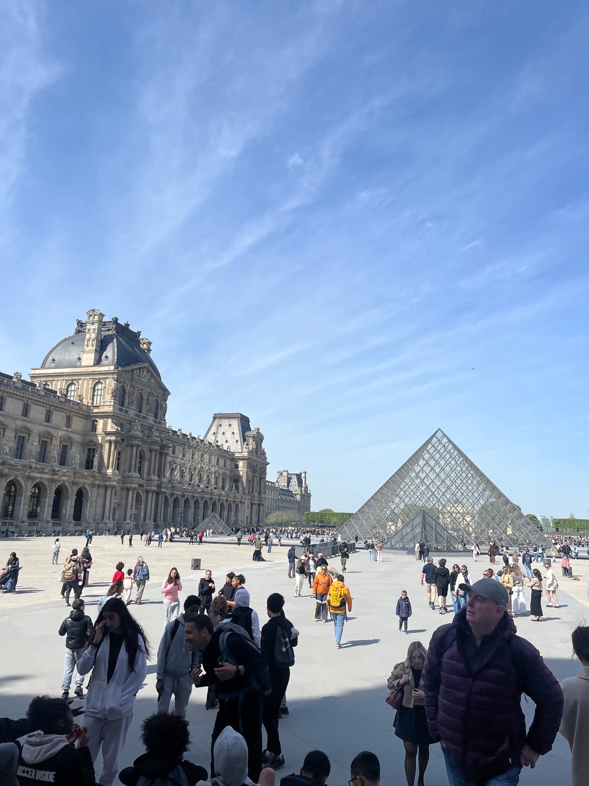 Crowds gather at Louvre Museum plaza under clear skies