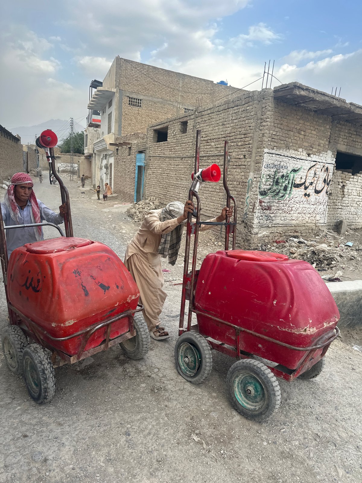 Two people pull red carts on unpaved Quetta street
