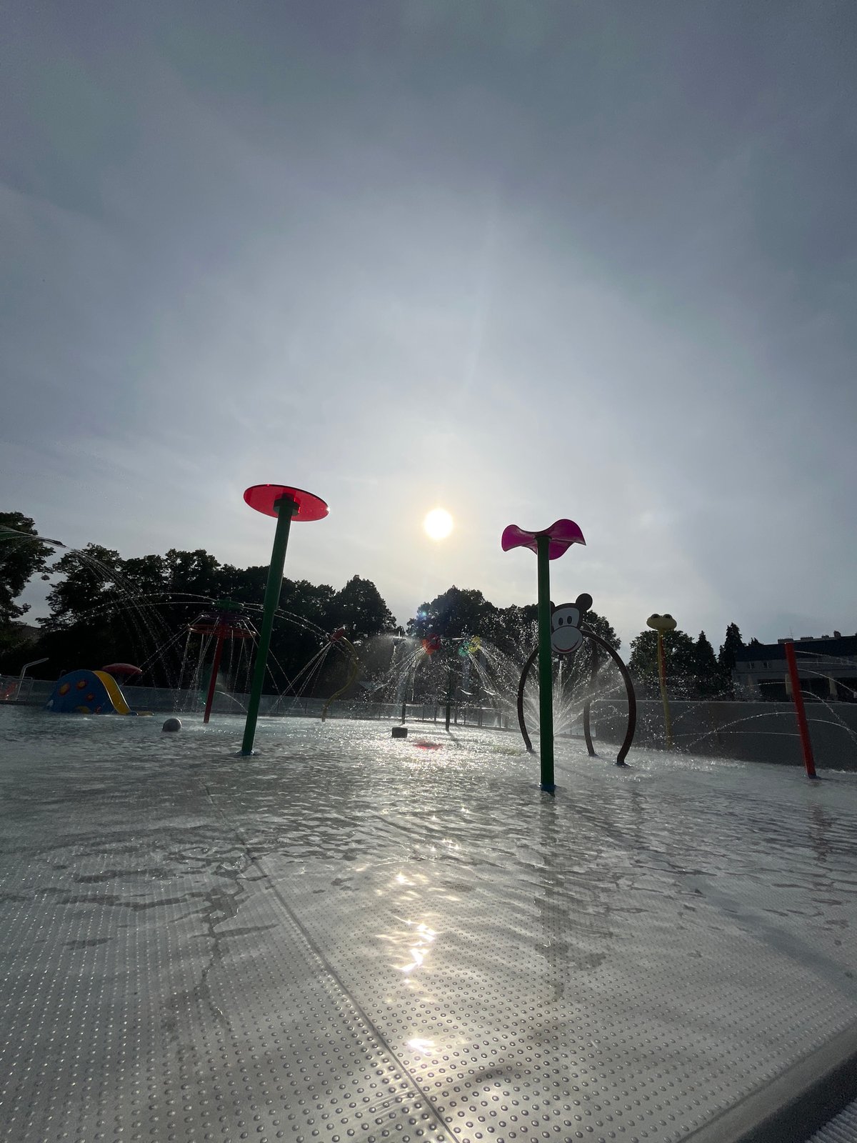 Outdoor pool and splash pad facility documented under varied sky
