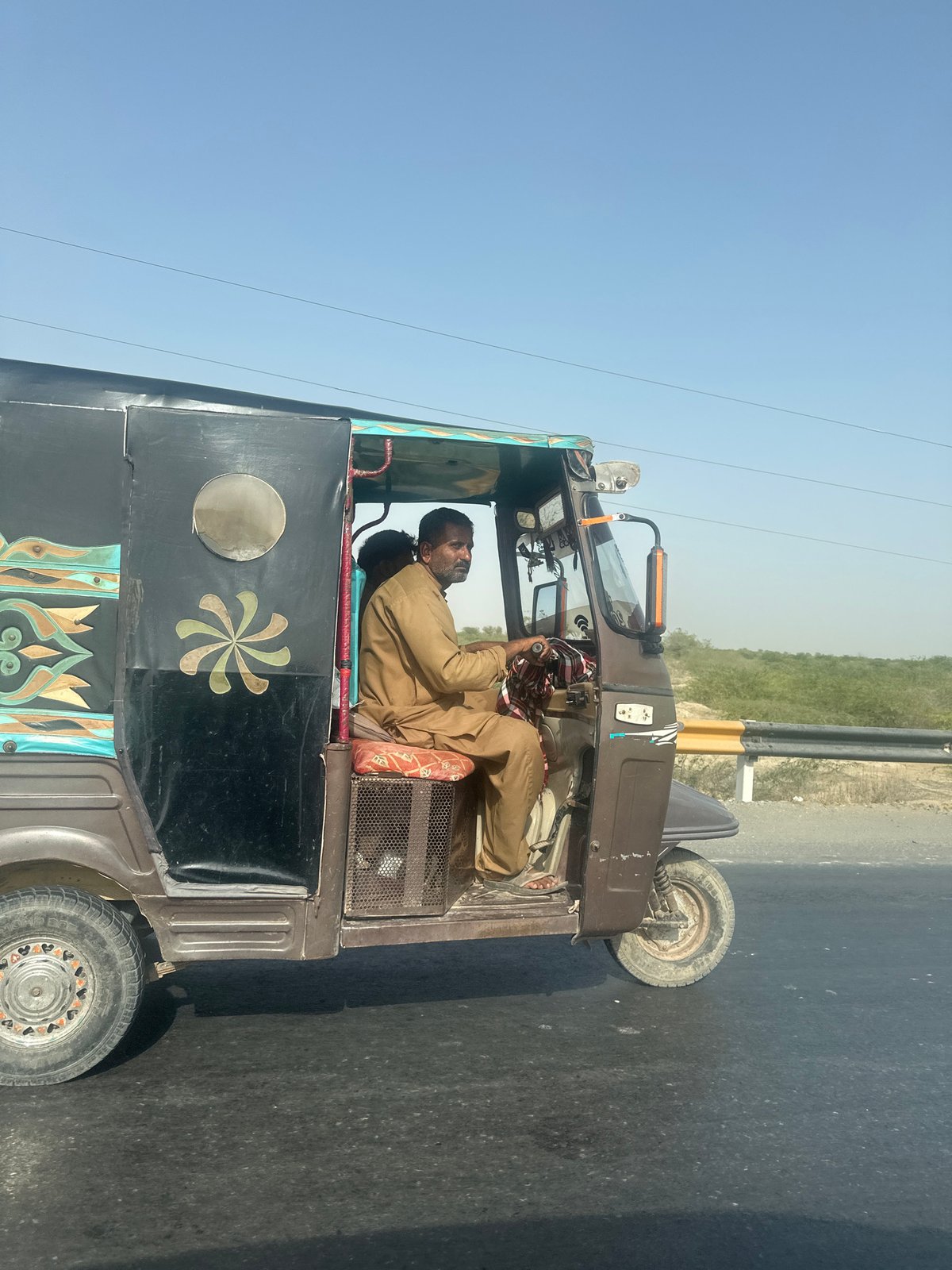 Decorated auto-rickshaw rolling down a sunny Pakistani road