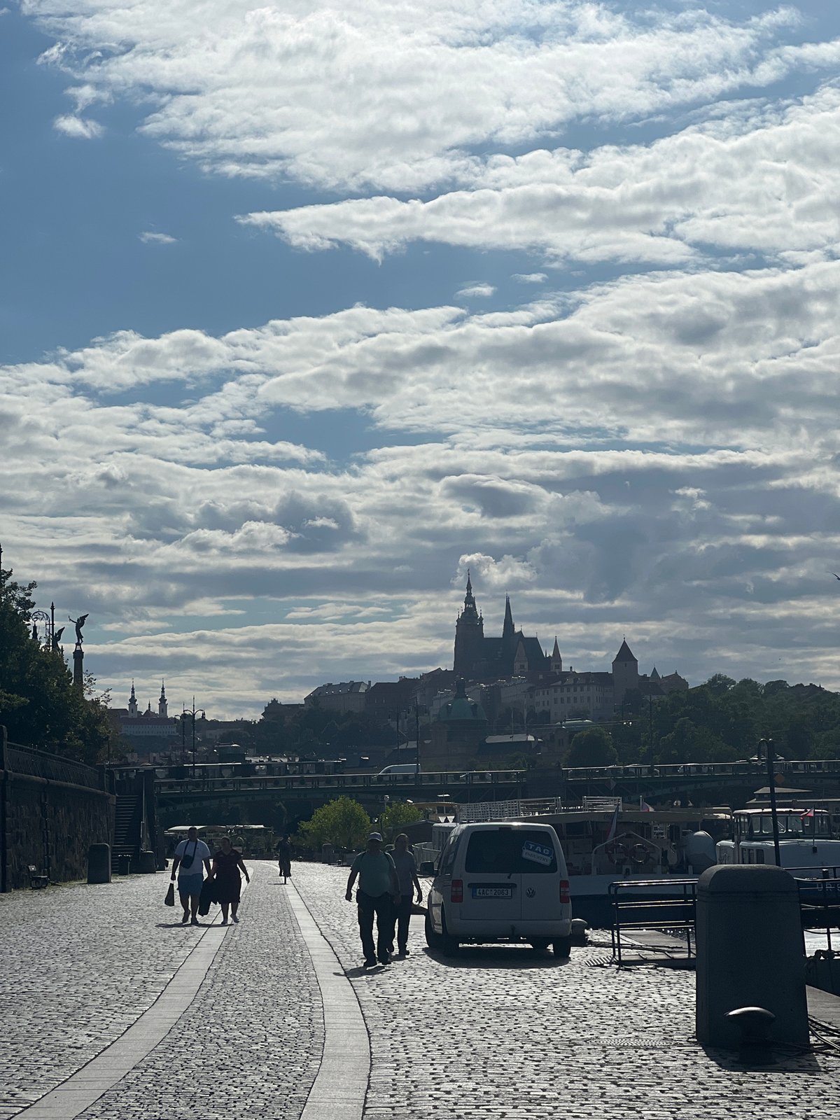 Strolling a cobblestone riverside path with city spires ahead