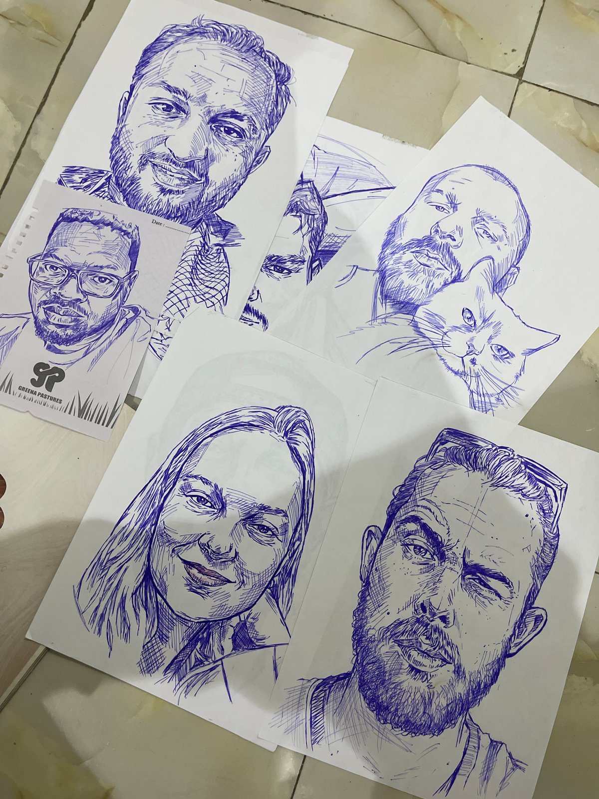 Blue ink portraits and sketches spread across a floor in Abuja