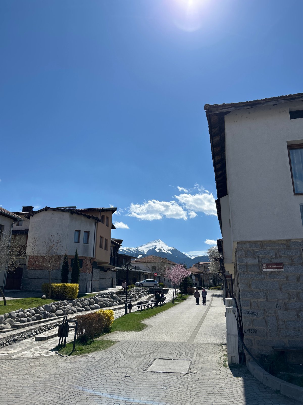 Pedestrians stroll through sunny Bansko with mountain backdrop