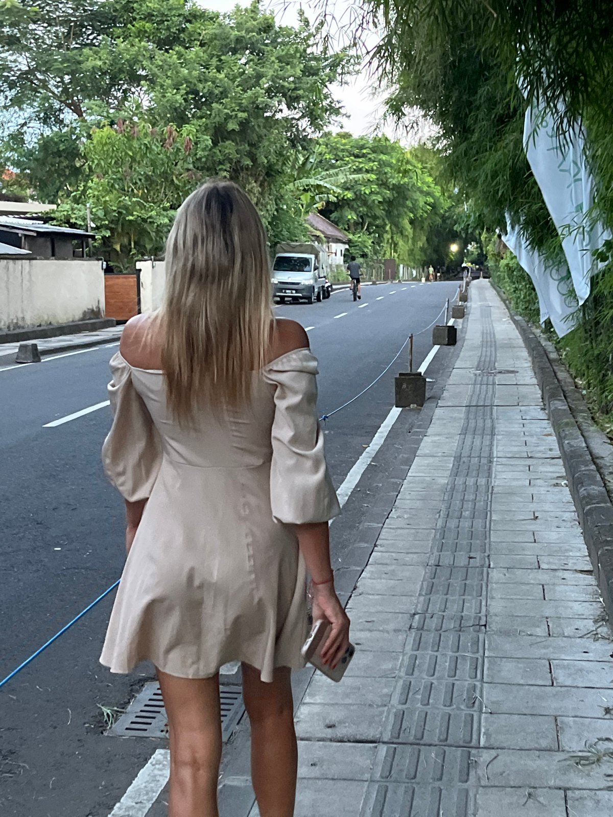 Woman walks Indonesian street amid tropical greenery, passing truck