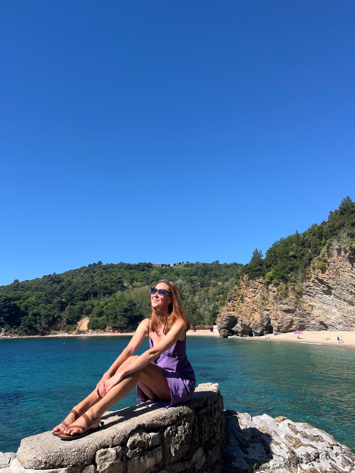 Woman sunbathes on rocky cliffs overlooking Budva beach