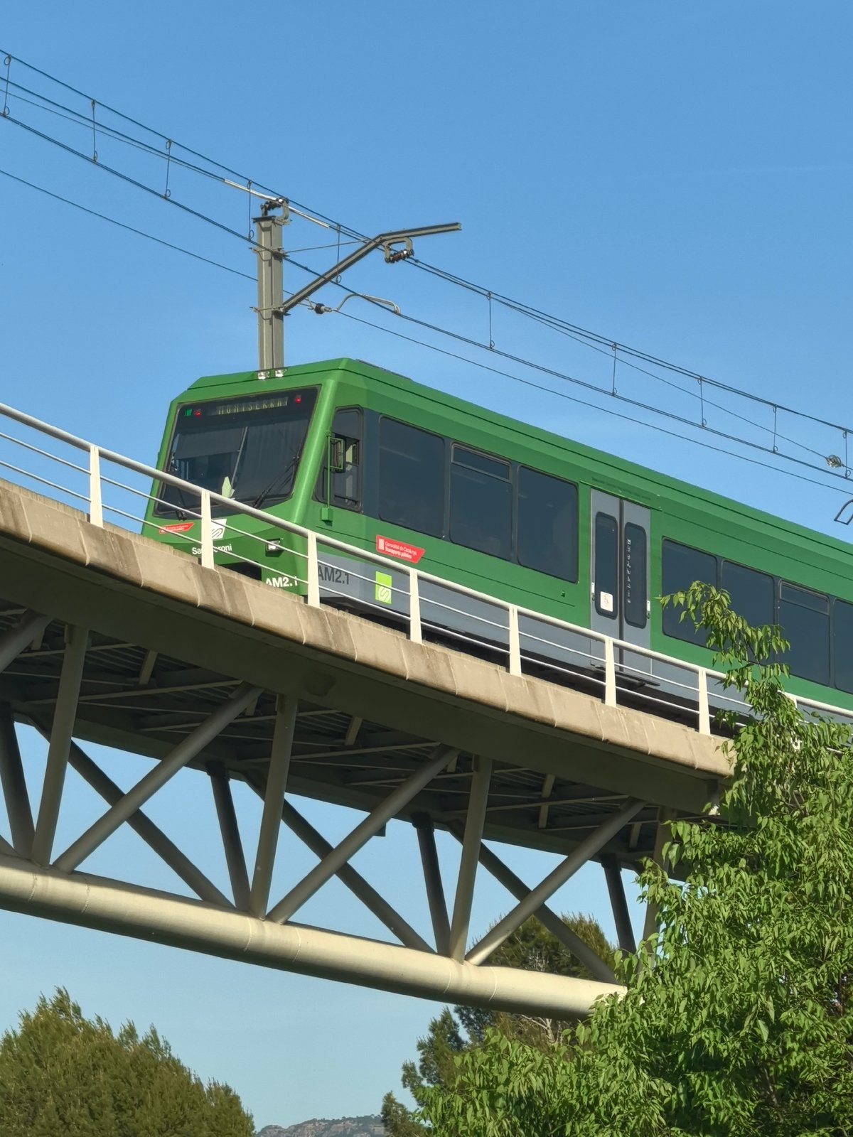 Green electric train crosses elevated bridge in Monistrol de Montserrat