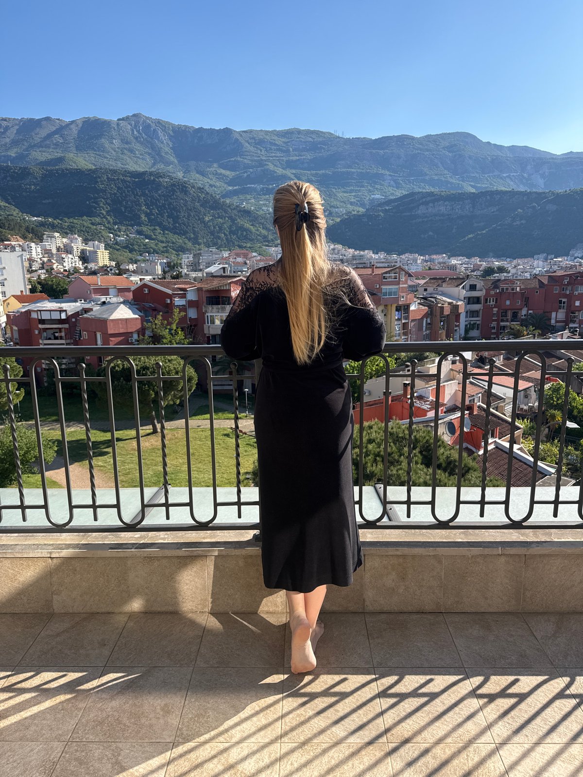 Woman in black dress observed on Budva balcony overlooking mountains
