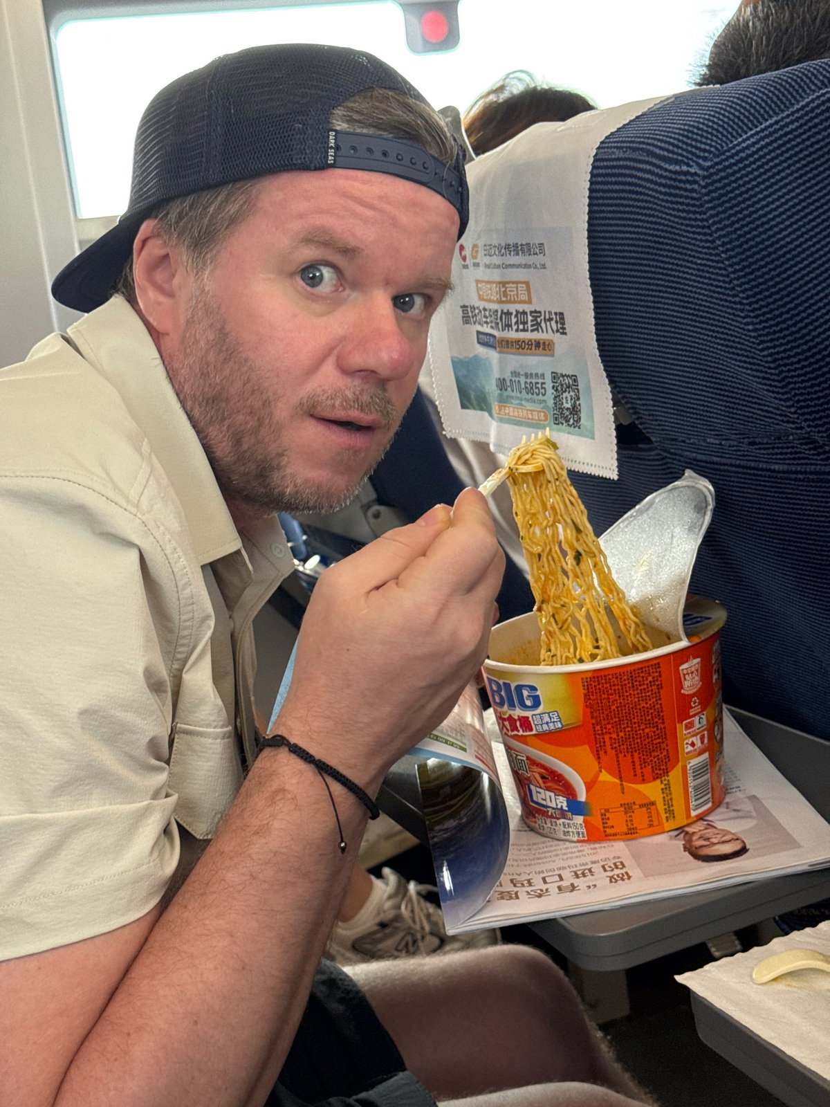 Surprised mid-bite with instant noodles on a flight over China