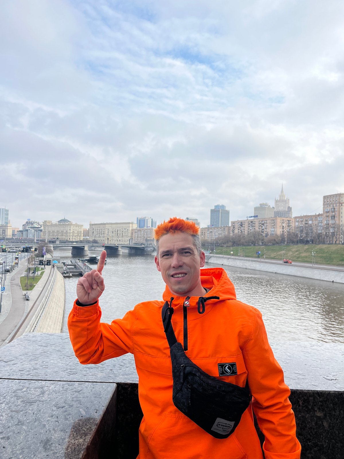 Man in orange jacket observed on platform overlooking city river