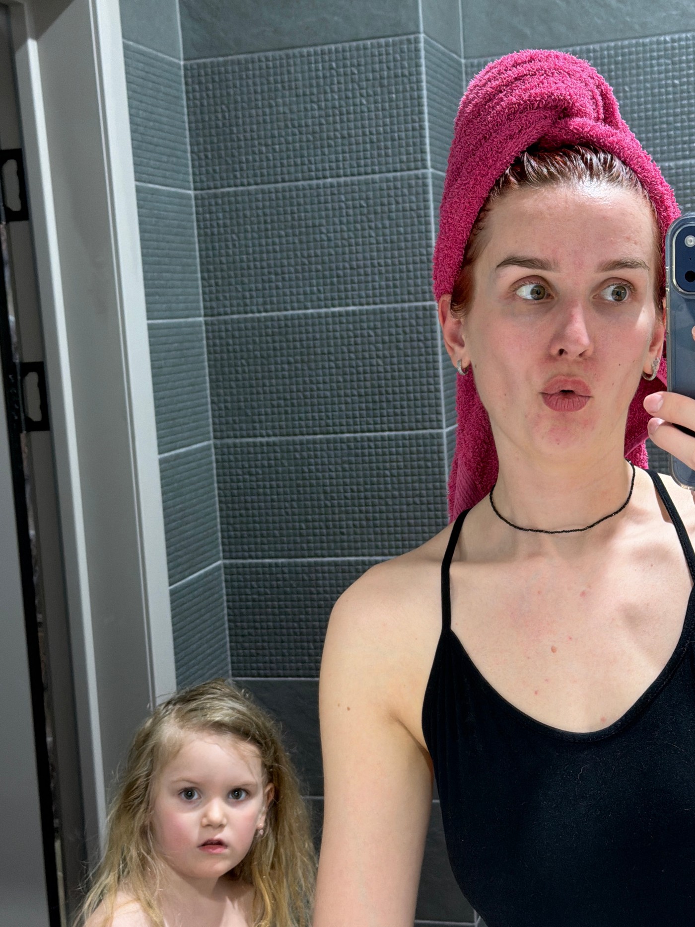 Woman takes bathroom selfie with child visible in mirror