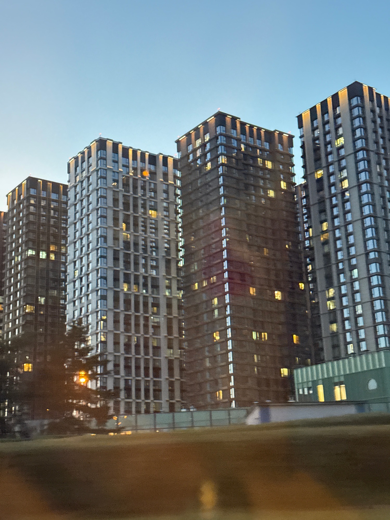 City high-rises tower overhead as lights flicker on at dusk