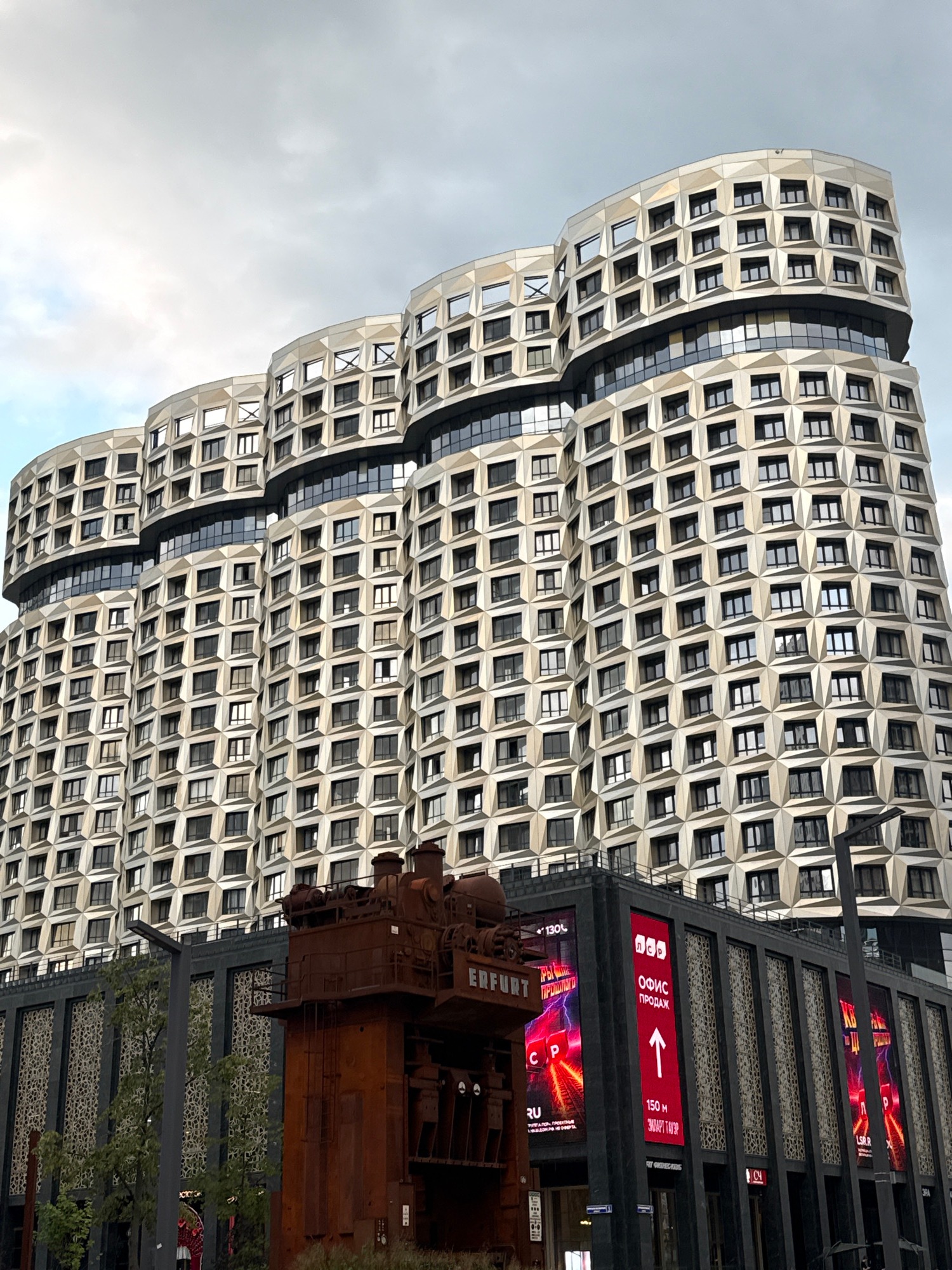 Modern architecture meets weathered industrial sculpture in an urban setting