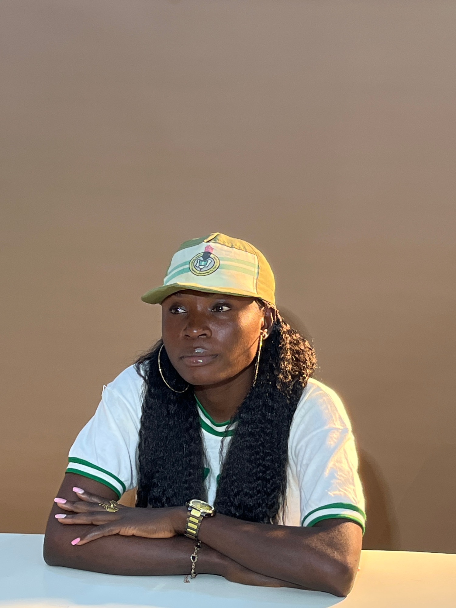 Seated figure in green-trimmed outfit, arms crossed, smiling