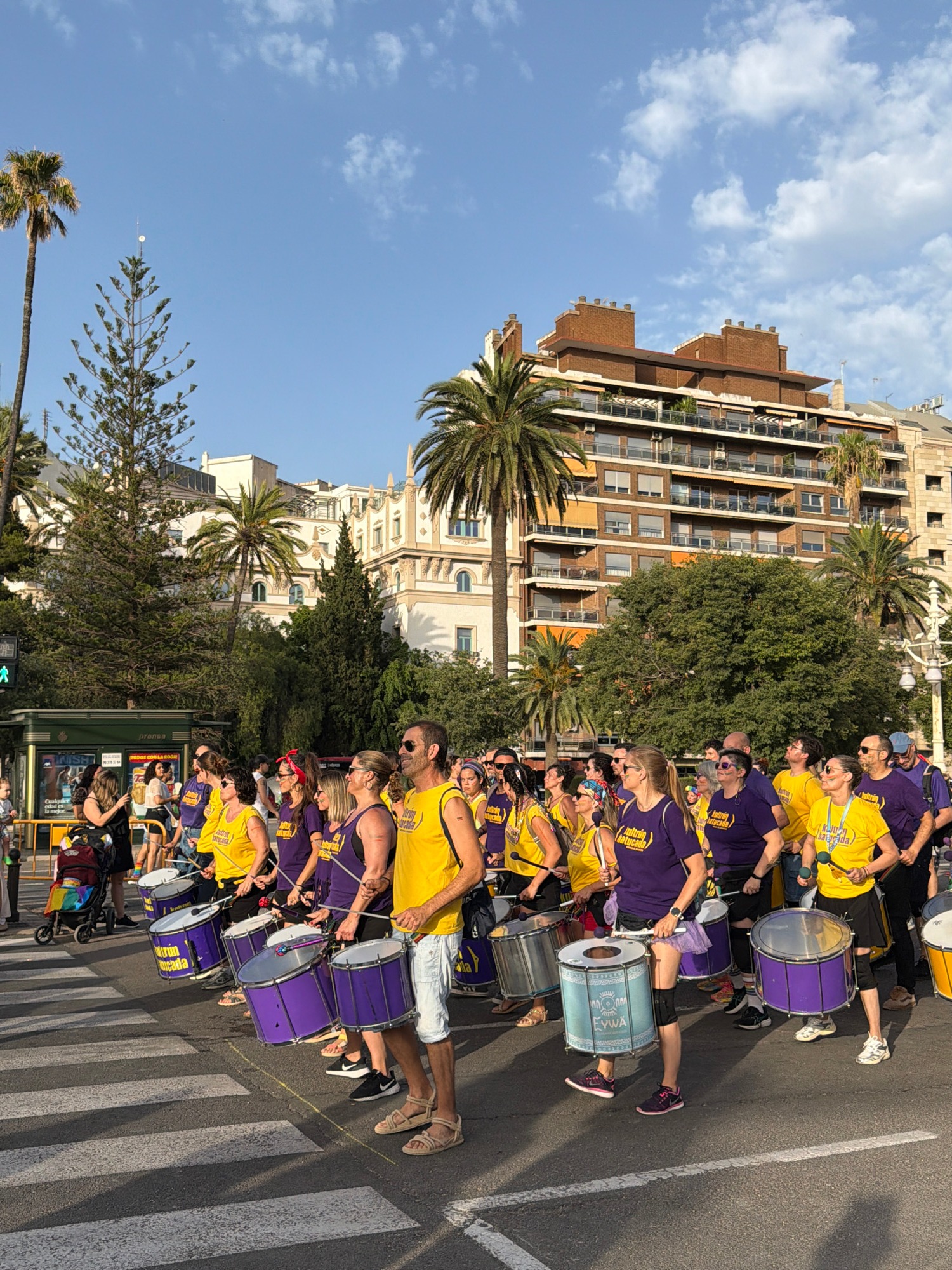 Pride parade crosses city bridge with flags, drums, and festive crowds
