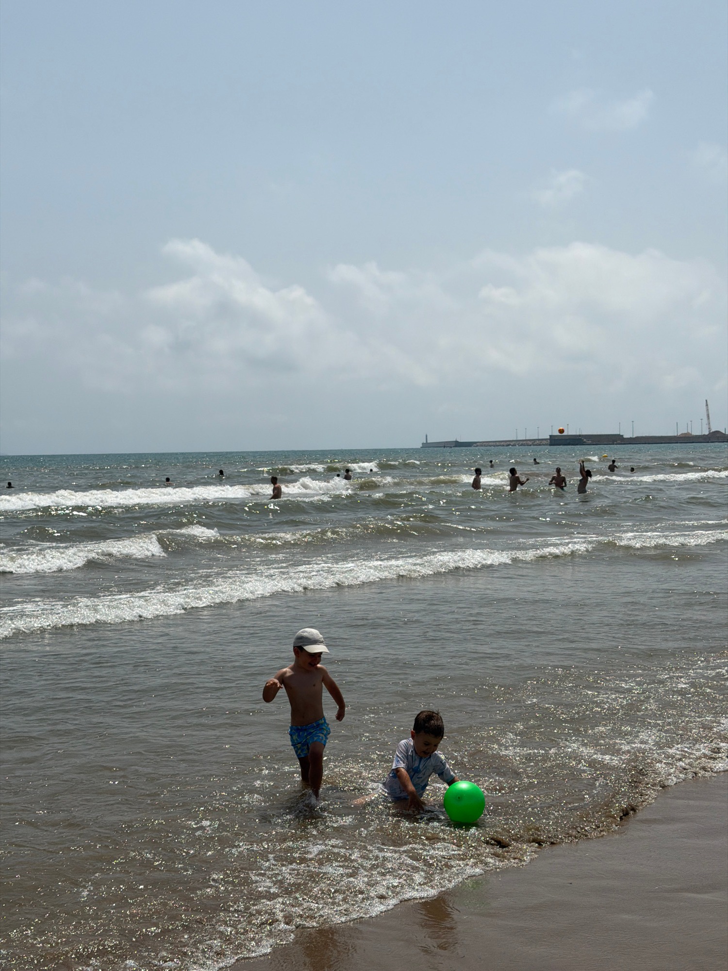 Crowded beach day with swimmers, kids, and street scenes nearby