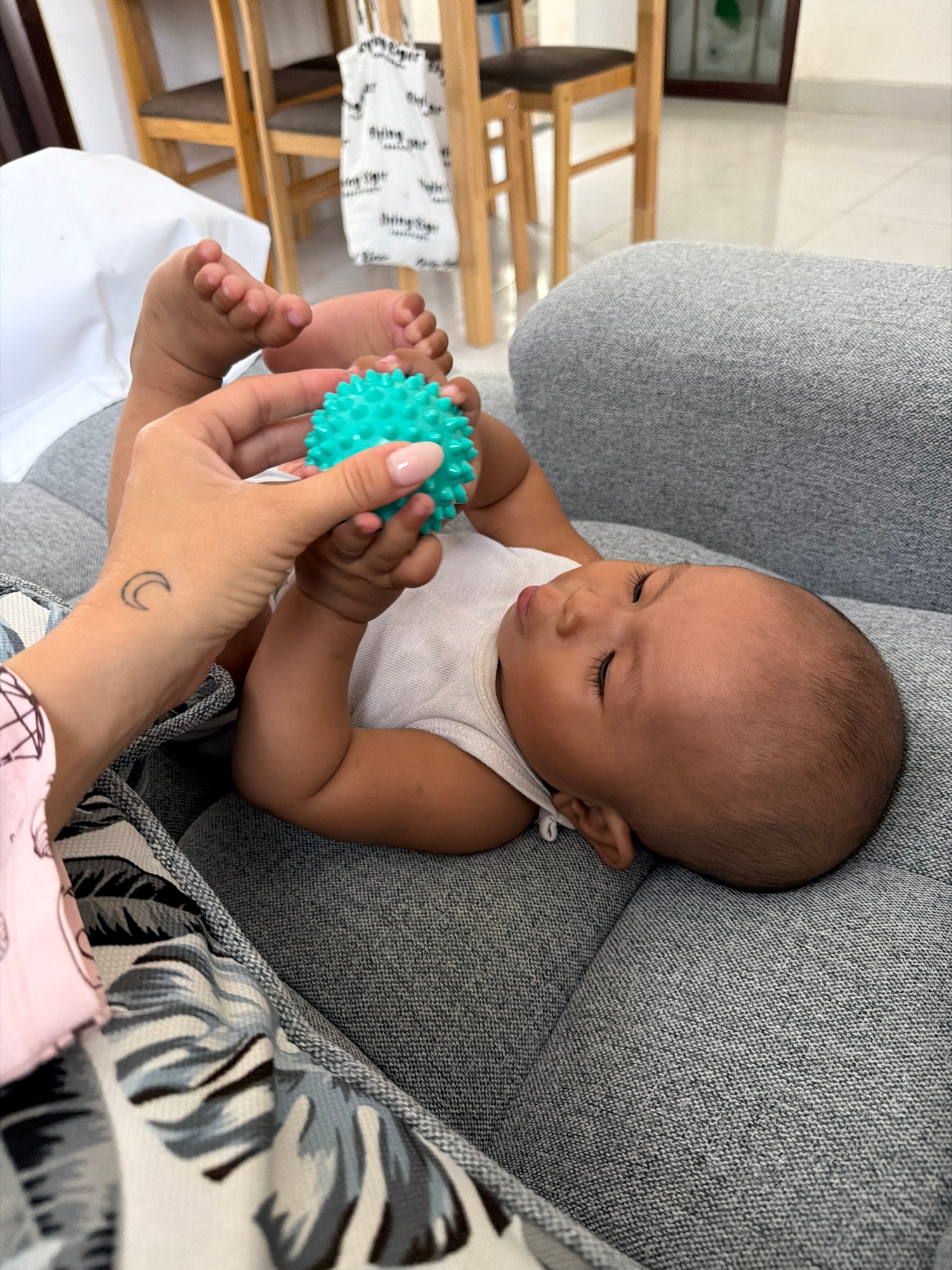 Baby and Pomeranian share a couch with a teal spiky ball