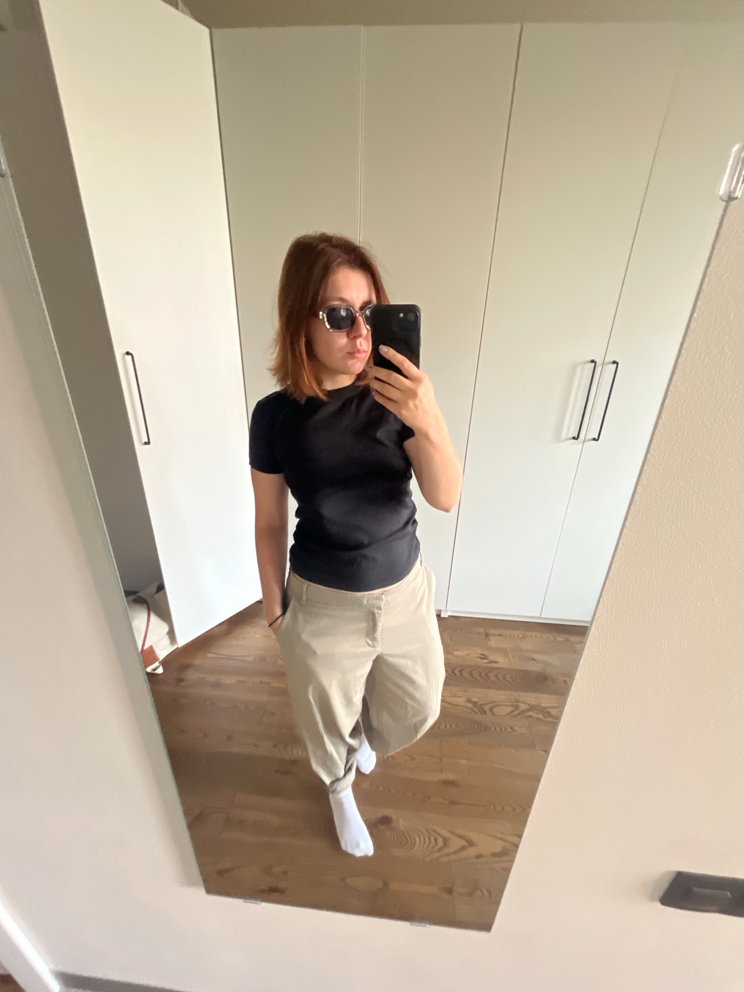 Mirror selfie in black tee, tan pants, and shades