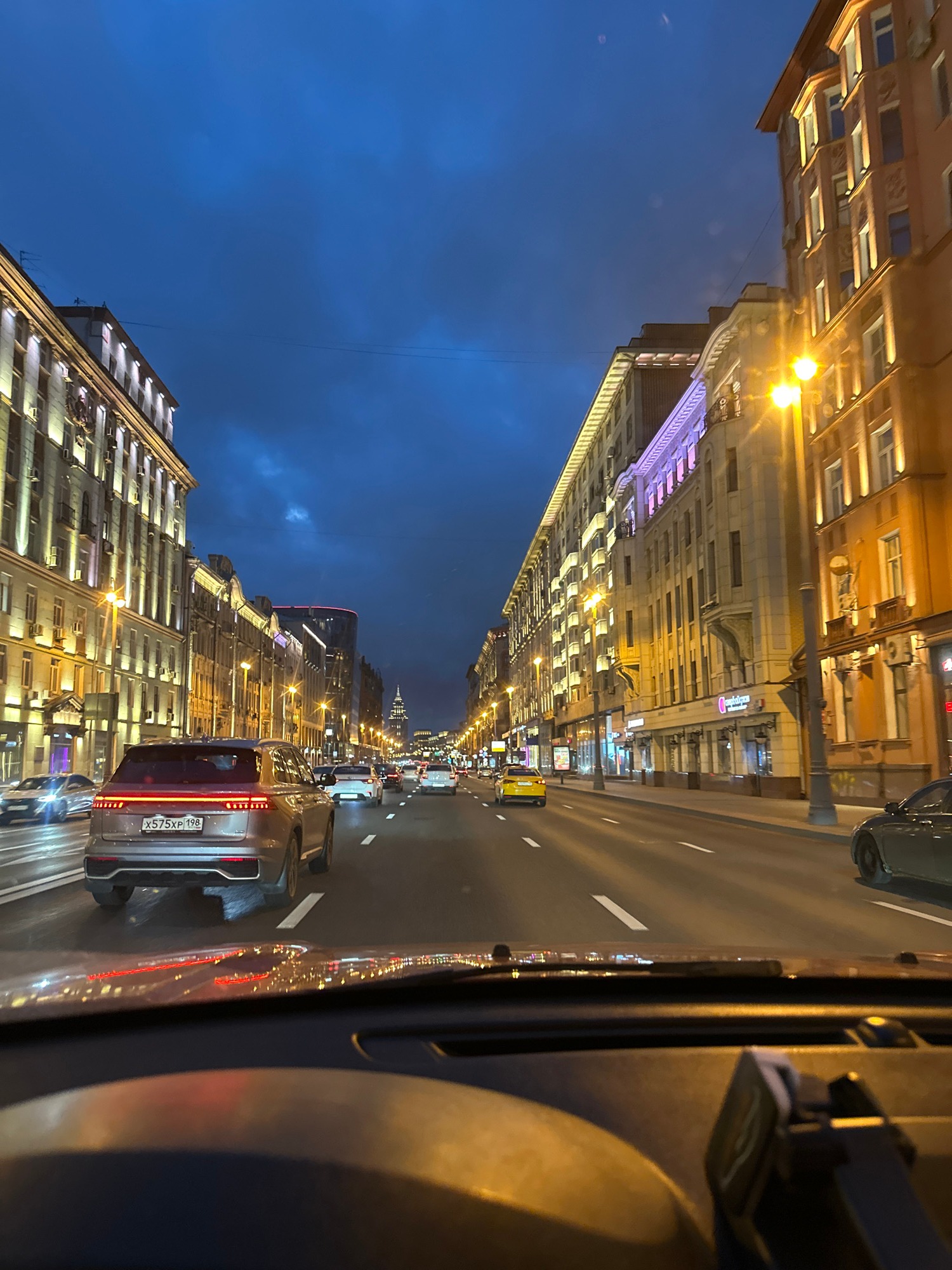 Cruising a lit city boulevard at dusk under heavy clouds