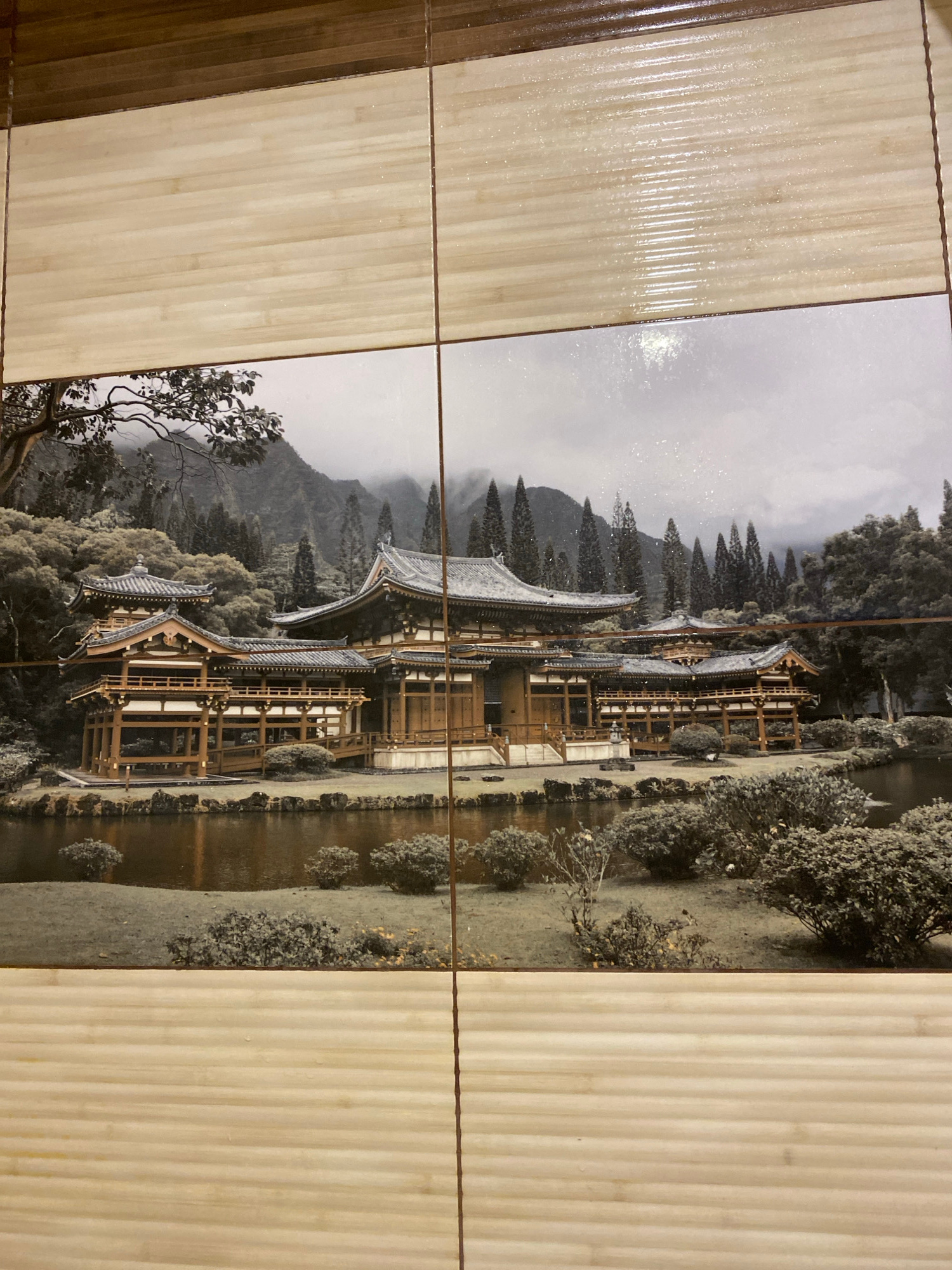 The image shows a tiled wall, likely in a bathroom or kitchen, featuring a printed mural of a traditional Japanese temple complex situated beside a body of water. The mural is rendered in a black and white, sepia-toned style. The temple structures are elaborate with multiple tiered roofs, wooden beams, and intricate architectural details. In the background, lush trees and misty mountains form a serene landscape. The surrounding tiles above and below the mural have a light wood-grain pattern. The image was captured on March 25, 2024, at 11:32 AM. There is no indication of the location being Kharkiv, Ukraine, as the image depicts a scene of Japanese architecture and landscape.