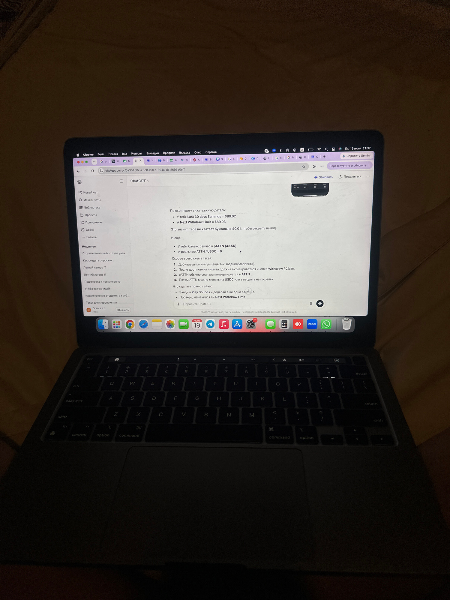 A laptop is open and displaying the ChatGPT interface. The screen shows a conversation with ChatGPT regarding earnings and withdrawal limits. On the left side of the screen, a sidebar lists "New chat", "Search chats", "Library", "Projects", "Apps", and "More". The laptop's keyboard is visible in the foreground, illuminated by the screen's glow. The image is taken from a slightly elevated angle, looking down at the laptop. The background is dark and appears to be a textured surface, possibly a bed or sofa. The overall scene is dimly lit, suggesting it may be nighttime. There is no indication of the location being North Kuta, Indonesia.