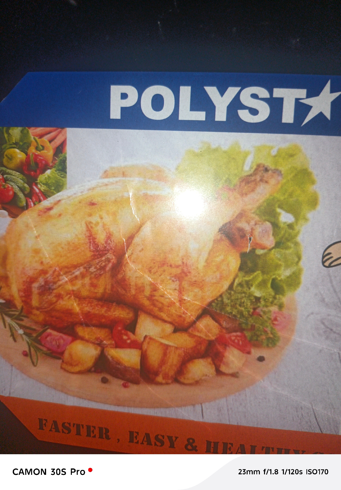 The image displays a close-up of a food advertisement. The advertisement features a roasted chicken served with potatoes and a side salad. Above the food image, the brand name "POLYST" is visible in large white letters against a blue background, with a star icon to the right of the name. Below the food image, text reads "FASTER, EASY & HEALTHY". At the bottom of the image, there is text indicating "CAMON 30S Pro" and camera settings "23mm f/1.8 1/120s ISO170". The background of the advertisement appears to be a light gray wood texture. There is no indication of a city or specific location.