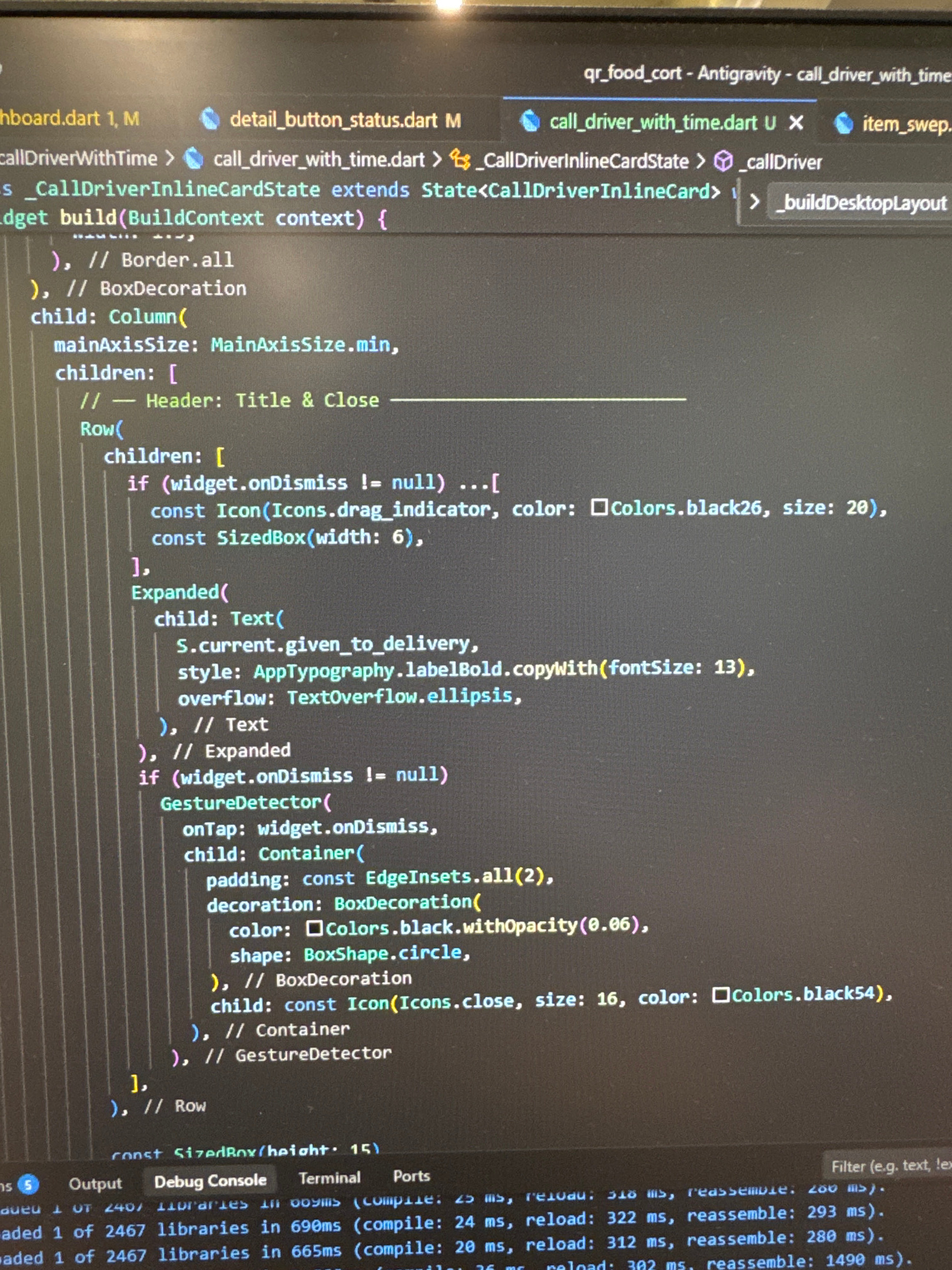 The image shows a close-up, angled shot of a computer screen displaying code. The code appears to be written in Dart, indicated by the file extensions (.dart) and syntax. Specifically, the code is from a file named "call_driver_with_time.dart" and is within a widget build method.
The code snippet includes elements like `Column`, `Row`, `Expanded`, `Text`, `Icon`, and `GestureDetector`, suggesting a user interface is being constructed. There are comments like "// Header: Title & Close" and "// Border.all", which provide context to the code's purpose.
At the bottom of the screen, there are tabs for "Output", "Debug Console", "Terminal", and "Ports", typical of an Integrated Development Environment (IDE). Below these tabs, there is information about library loading times, such as "loaded 1 of 2467 libraries in 690ms".
The lighting suggests the photo was taken in a dimly lit room, with the primary light source being the computer screen itself. No people, subjects, or specific interactions are visible in the image, beyond the code on the screen. The environment is simply the surface of a screen reflecting its digital content. There is no information in the image that could place this scene in Yerevan, Armenia.