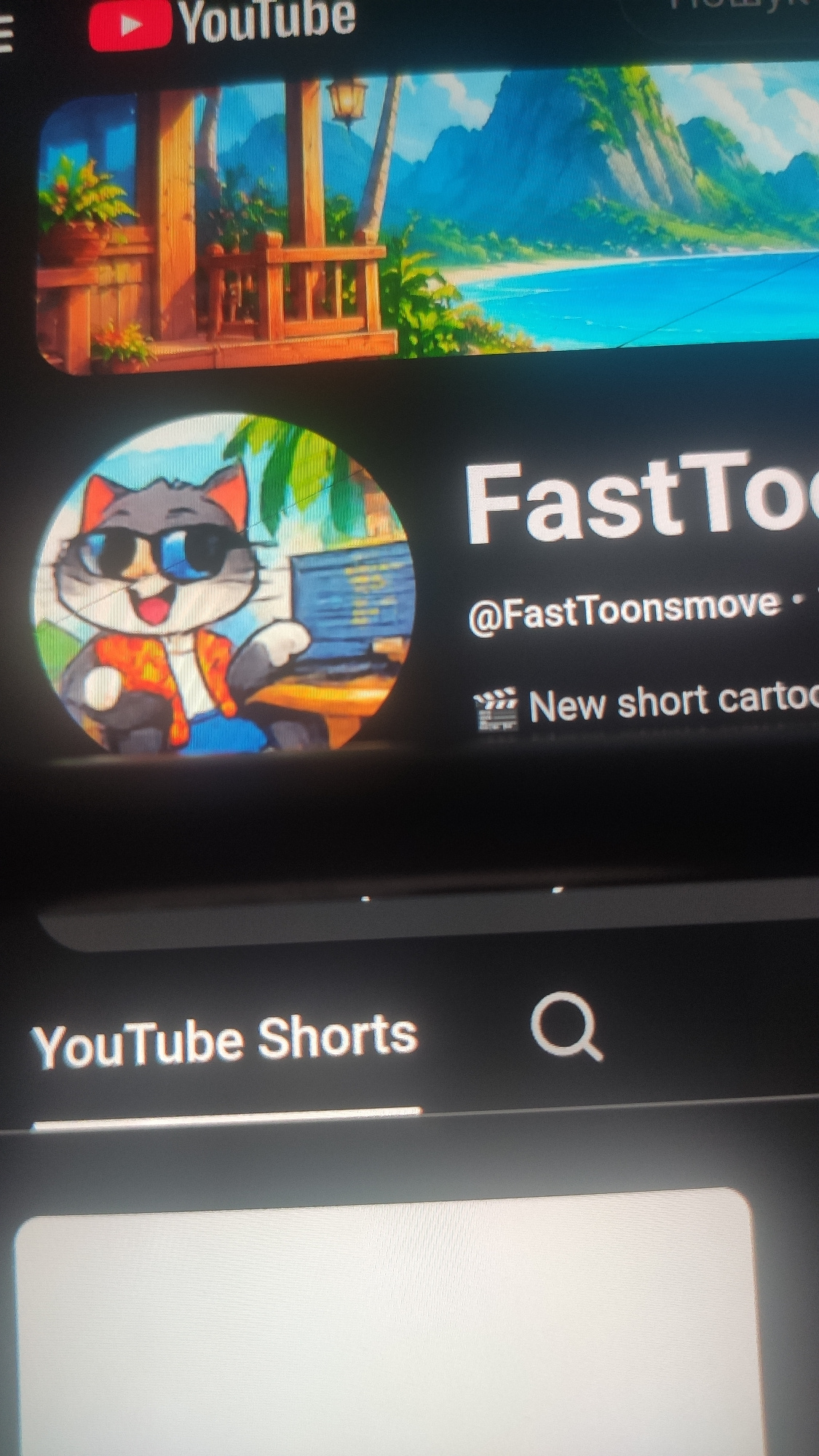 The image shows a vertical display on a screen, likely a mobile phone or tablet, showing content from YouTube Shorts. The dominant visual element on the left is a thumbnail for a YouTube channel named "FastToons". The thumbnail features an animated cartoon cat wearing sunglasses and a colorful outfit. To the left of the thumbnail, the YouTube logo is visible, along with the text "YouTube" written vertically.
Above the "FastToons" channel name, there is text that reads "@FastToonsmove" followed by a period. Further to the right, there is additional text that says "New short cartoo". A small film reel icon is also present next to this text.
The background of the "FastToons" thumbnail appears to be a scenic view of a tropical landscape with lush greenery and a body of water. There is also a wooden structure resembling a balcony or deck.
On the right side of the screen, there is a search icon and the text "YouTube Shorts" written vertically. A blank white area suggests a video player or another content section.
The overall impression is a digital interface displaying a YouTube Shorts channel promotion, with a focus on animated content. The scene depicted in the thumbnail suggests a bright, sunny day, likely outdoors. The specific location "Madrid, Spain" is provided as context, but there are no visual cues in the image itself that directly indicate this location. The image is captured from an angle, causing the text and elements to appear tilted.