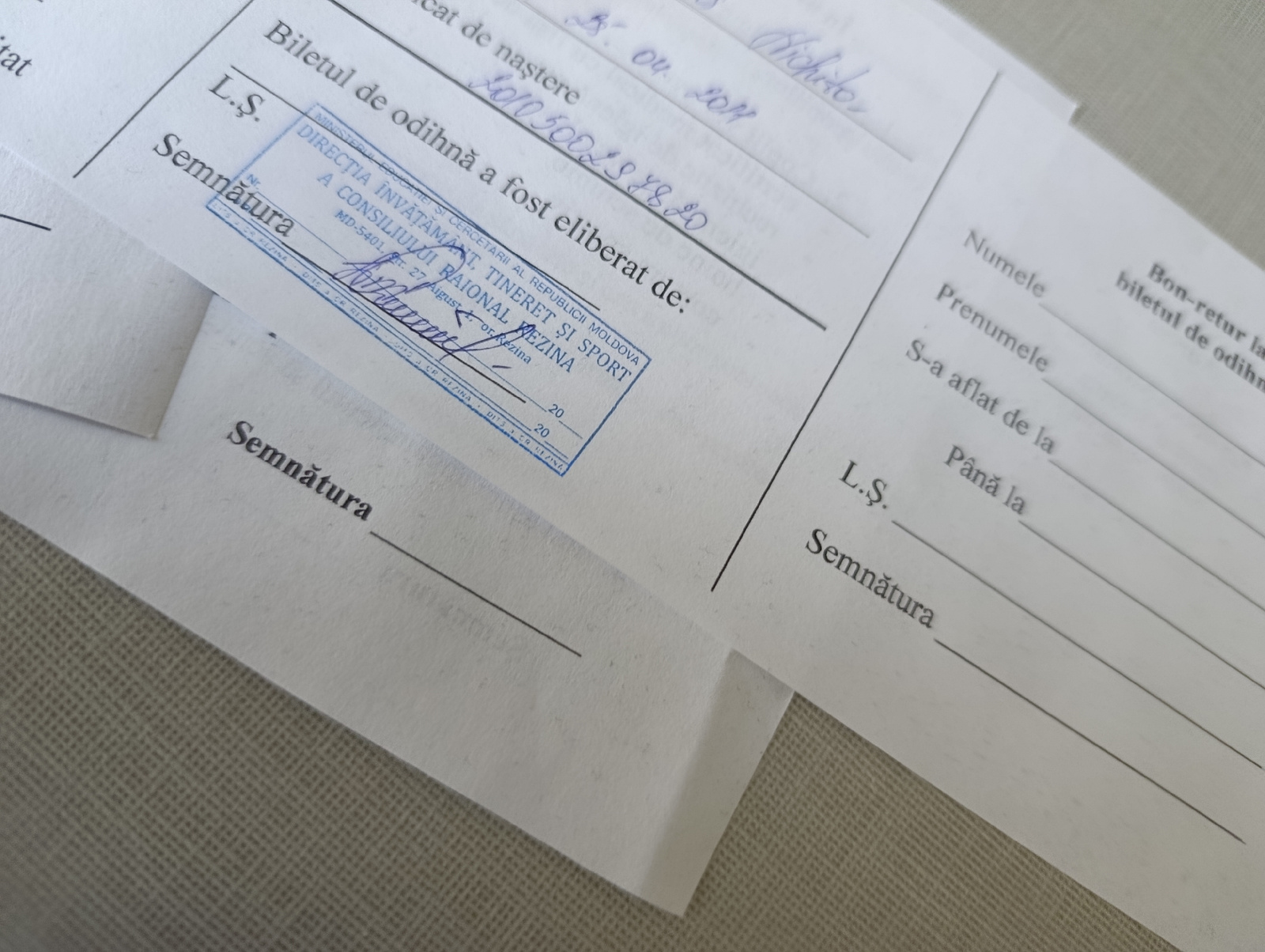 The image shows a document, likely a certificate or permit, with handwritten and stamped text. The stamped text indicates that the document was issued by the "DIRECȚIA ÎNVĂȚĂMÂNT, CERCETĂRI AL REPUBLICII MOLDOVA A CONSILIULUI RAIONAL TINERET ȘI SPORT OR REZINA." This translates to "Directorate of Education, Research of the Republic of Moldova of the Council of Youth and Sport of Rezina District." The stamp also includes a date, "ST. 27 August, 2012," and what appears to be a signature. There are handwritten entries on the document, including a number "1010 500218820" and a date "B. 04. 2011." The document also has fields for "Semnătura" (Signature), "L.S." (Locus Sigilli - Place of the Seal), "Numele" (Name), "Prenumele" (Surname), and "S-a aflat de la" (Has been from) and "Până la" (Until). The document is lying on a textured surface, possibly a table or desk.