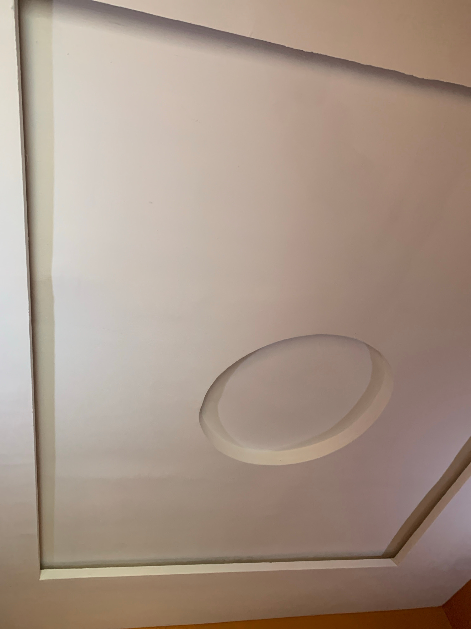 A white, recessed ceiling features a central oval indentation. The ceiling is framed by a rectangular recess with beveled edges. The overall impression is one of modern interior design. The scene is indoors and appears to be a room with a ceiling.