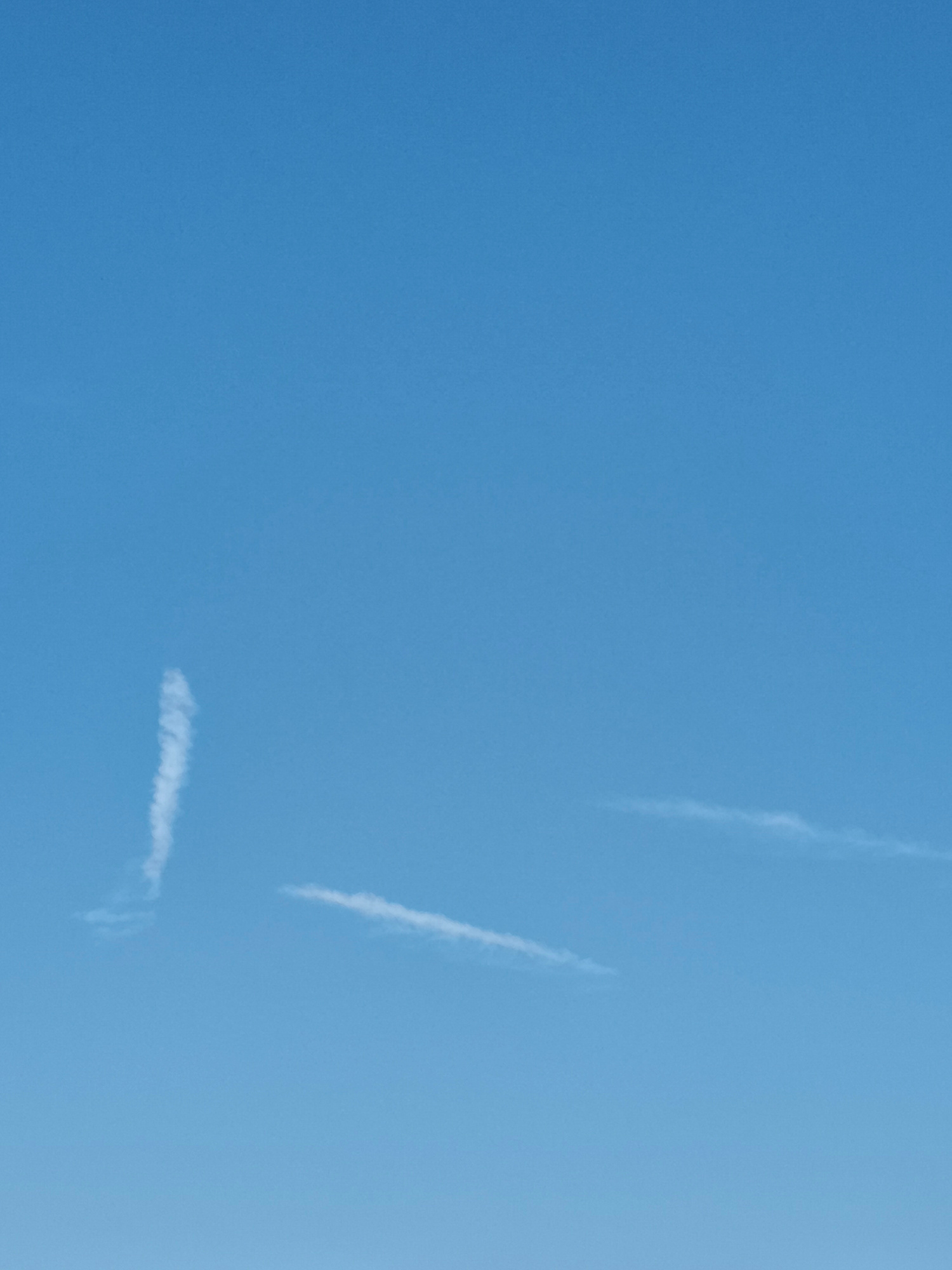 The image displays a clear blue sky with two wispy clouds. One cloud is positioned in the upper left quadrant, appearing as a vertical streak. The second cloud is located in the lower right quadrant, stretched horizontally across the frame. No people, objects, or identifiable structures from Georgsmarienhütte, Germany are visible in this image. The scene is entirely dominated by the sky and the faint cloud formations.