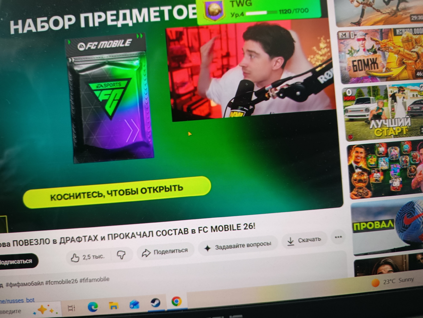 The image shows a computer screen displaying a YouTube interface. On the left side, a large banner reads "НАБОР ПРЕДМЕТОВ" (Item Pack) with a graphic of a FC Mobile pack. Below that, in a yellow oval, is the text "КОСНИТЕСЬ, ЧТОБЫ ОТКРЫТЬ" (Tap to open). To the right of the banner, a smaller video window shows a young man speaking into a microphone, with a red-tinted background and golden confetti. The main part of the screen displays a YouTube video title "ОВА ПОВЕЗЛО в ДРАФТАХ и ПРОКАЧАЛ СОСТАВ в FC MOBILE 26!" (Lucky in Drafts and Upgraded Squad in FC MOBILE 26!). Below this, there are icons for likes (2.5k), dislikes, sharing, asking questions, and downloading. Further down are hashtags related to FC Mobile and a URL for a bot. The bottom of the screen shows taskbar icons for various applications, including Google Chrome. The weather widget in the bottom right corner indicates "23°C Sunny". There is no discernible information in the image that places it in the city of Rezina, Moldova.