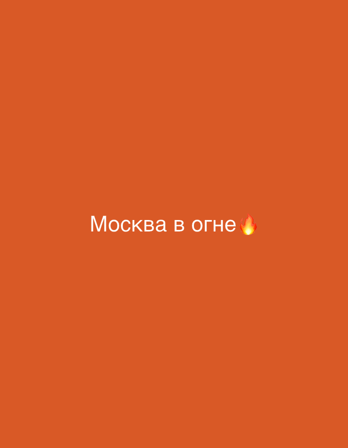 The image is a simple, minimalist graphic with a solid orange background. Centered in the frame, white text reads "Москва в огне" which translates to "Moscow on fire". To the right of the text is a small, stylized flame emoji. There are no people, objects, or discernible environmental features present in the image, and it does not depict any location in Kaunas, Lithuania.