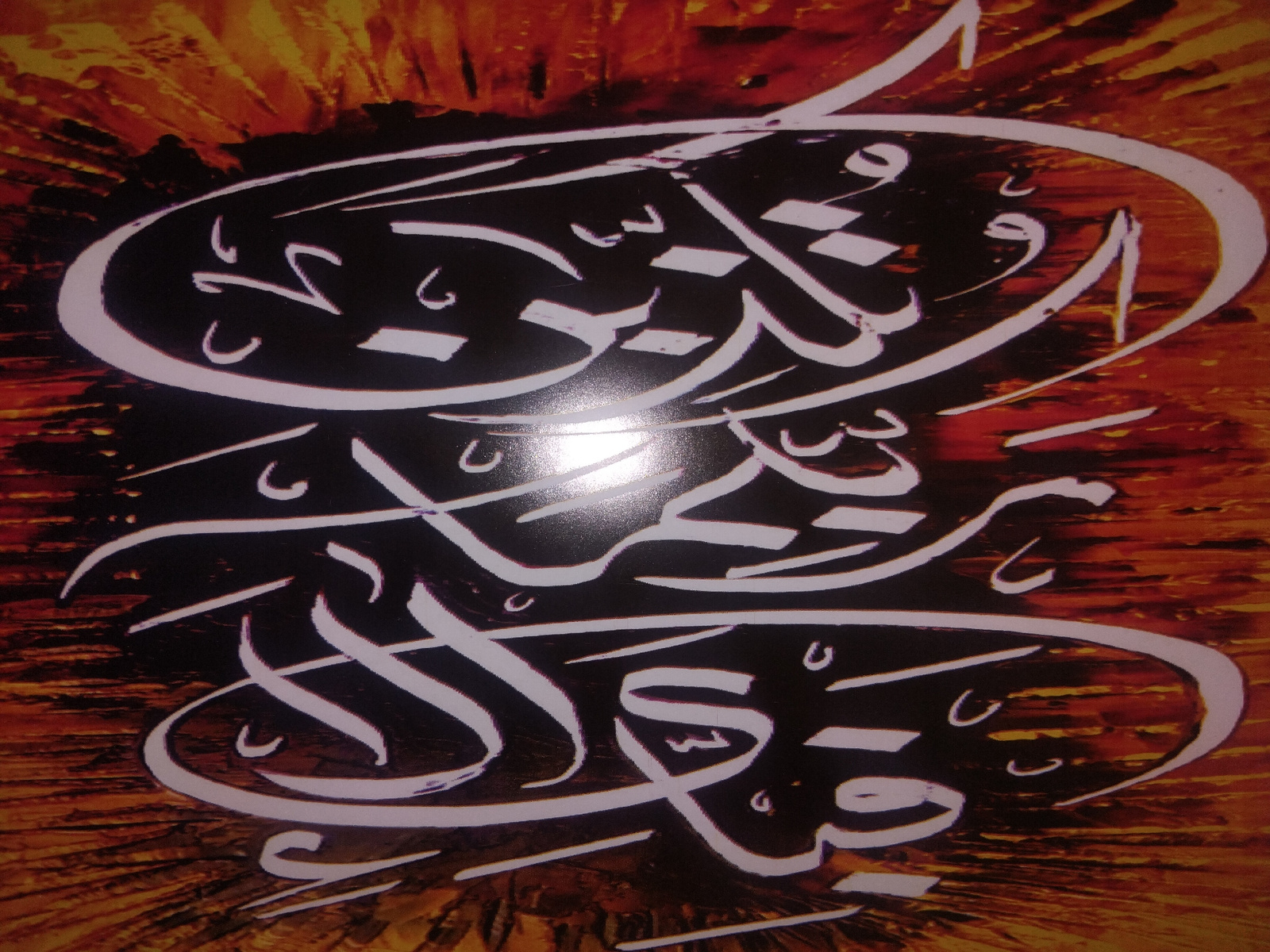 This is a close-up, vertically oriented image of white Arabic calligraphy against a dark background that transitions to a fiery orange and yellow textured pattern, resembling brushstrokes or light rays. The calligraphy is elaborate and flowing, with thick white strokes forming curves and sharp angles. Diacritical marks, small dots, and strokes are visible, adding detail to the letters. The overall design is abstract and artistic, with no discernible figures, objects, or a specific scene. The background evokes a sense of warmth, intensity, or perhaps a sunrise or sunset effect.
The calligraphy itself is the primary subject. While the specific text is not definitively translated, the style suggests it could be religious or poetic in nature, common in Islamic art. The visual impression is one of dynamic movement and ornamental beauty. There are no clear indications of a specific time of day, weather conditions, or location cues beyond the artistic style of the calligraphy and the textured background. The emotions evoked are primarily aesthetic appreciation for the art form.