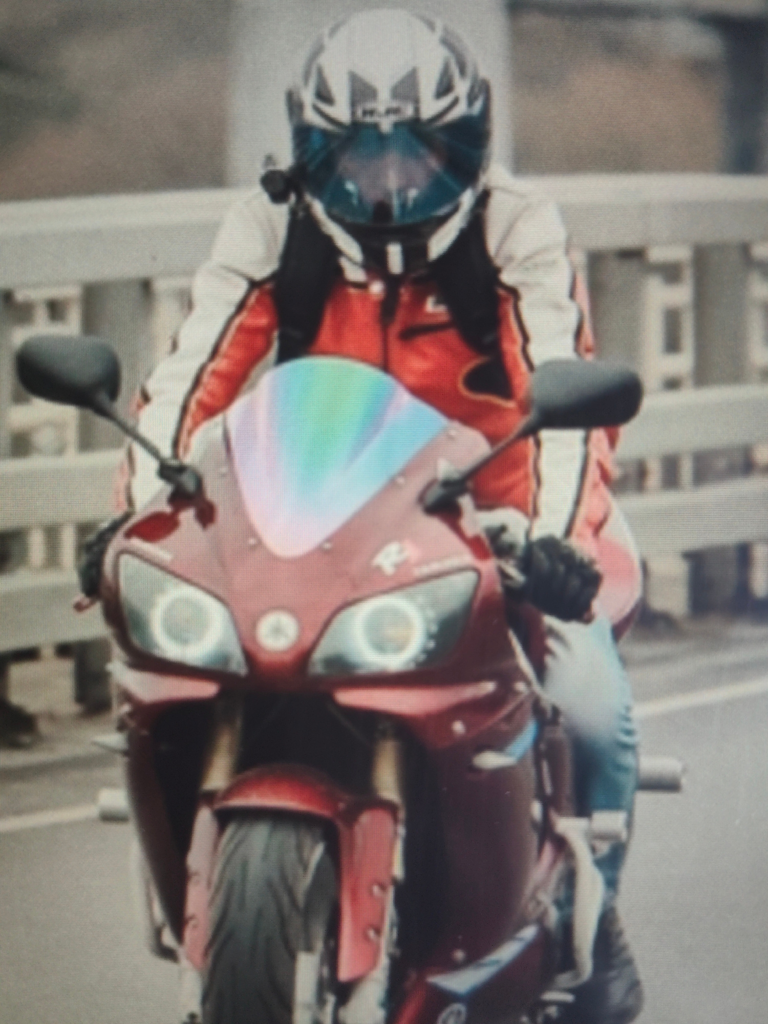 The image shows a person riding a motorcycle. The person is wearing a white and red motorcycle jacket, black gloves, and a white and black helmet with a blue visor. The motorcycle is red and appears to be a sportbike. It has a reflective windshield and two circular headlights. The rider is on a bridge, indicated by the railing in the background. The weather appears to be overcast, suggesting it might be a cloudy day. The scene is set in Bor, Russia. There is no discernible text in the image. The activity is simply riding a motorcycle, with no specific event or emotion conveyed.