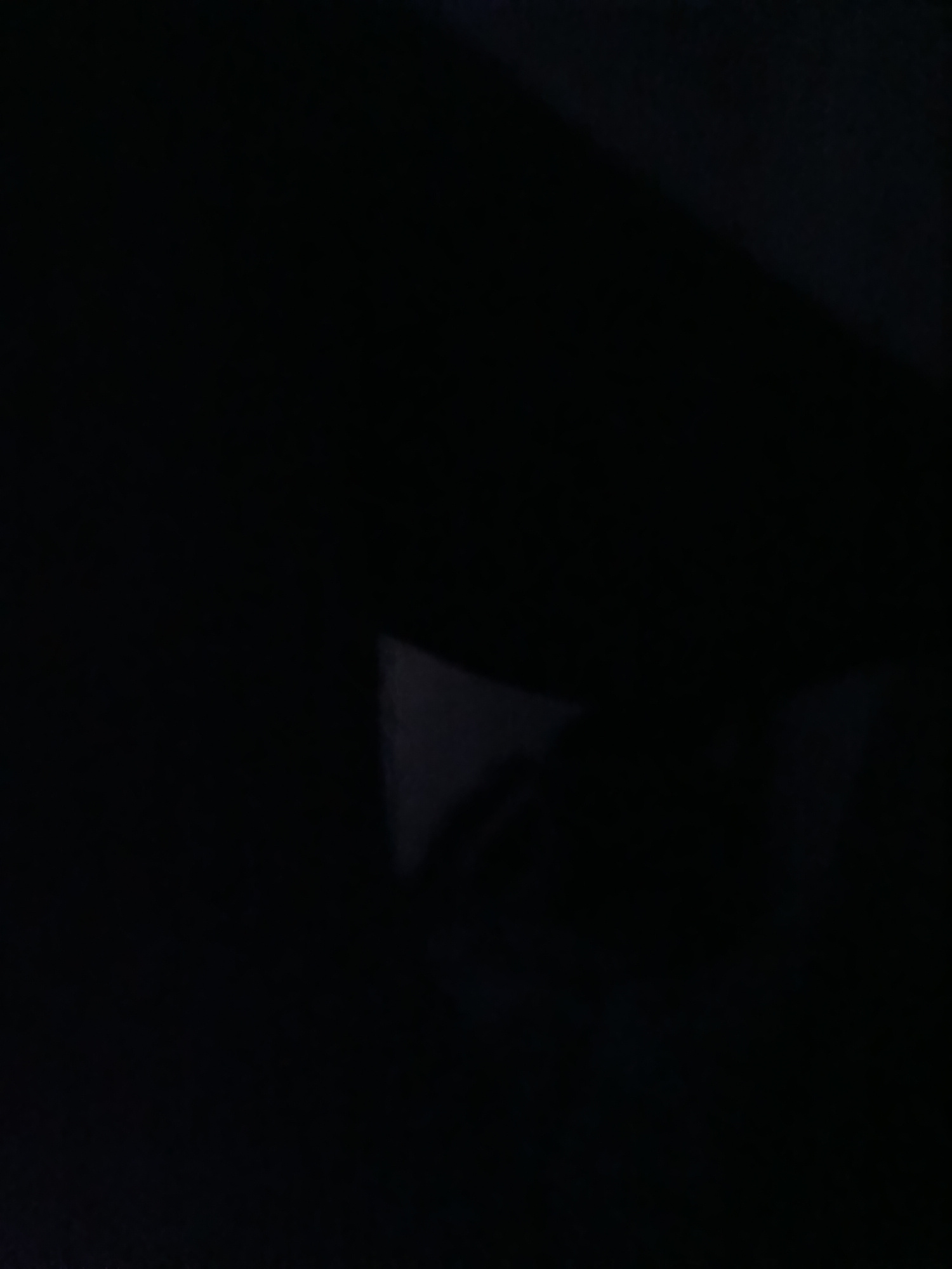 The image is dark and depicts a dimly lit room. A triangular object is visible in the lower right quadrant of the image. The object appears to be made of a light-colored material and is casting a shadow. The rest of the image is obscured by darkness.