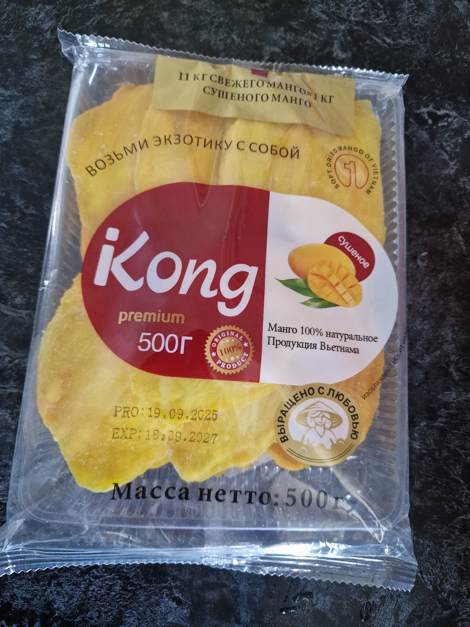 A package of dried mango slices is displayed on a dark, textured surface. The packaging is clear plastic, revealing the bright yellow fruit inside. A prominent red label on the front features the brand name "iKong" in large white lettering, followed by "premium" and "500г" in smaller text. Above this, a yellow banner reads "11 кг свежего манго = 1 кг сушеного манго". Another circular label with a stylized image of a woman wearing a conical hat and the text "Выращено с любовью" (Grown with love) is visible on the right side of the package. Below the main label, production and expiration dates are printed: "PRO: 19.09.2025" and "EXP: 18.09.2027". The text "Масса нетто: 500г" (Net weight: 500g) is printed at the bottom of the package. The image does not contain any information or context related to the city of Kursavka, Russia.