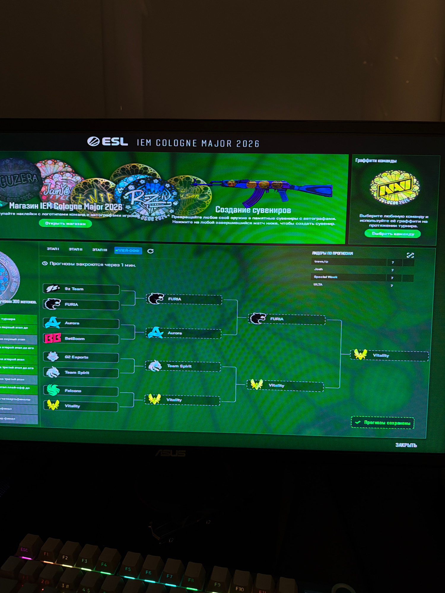 The image shows a computer screen displaying a video game interface related to "ESL IEM Cologne Major 2026." The screen features a tournament bracket with team names and logos, a shop section for virtual items, and a leaderboard for predictions. The overall aesthetic is dark with green and neon accents. The background is a dark, out-of-focus environment, possibly a room. A keyboard with illuminated keys is visible in the foreground, suggesting the image was taken from the perspective of someone using the computer. There is no visible indication of Toronto, Canada, within the image content.