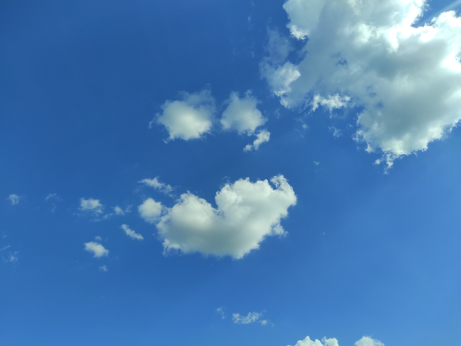 This is a media file featuring a bright blue sky with several white clouds scattered across it. The clouds vary in size and shape, with some appearing fluffy and cumulus-like, while others are more wispy. The sun is shining, as evidenced by the bright illumination of the clouds, particularly in the upper right portion of the image where a large cloud is brightly lit.
The scene depicts a clear day with good weather, suggesting it could be daytime, likely late morning or afternoon due to the bright sun. There are no people or discernible objects in the frame, focusing solely on the natural beauty of the sky. The overall impression is one of openness and tranquility. No text is visible within the image.