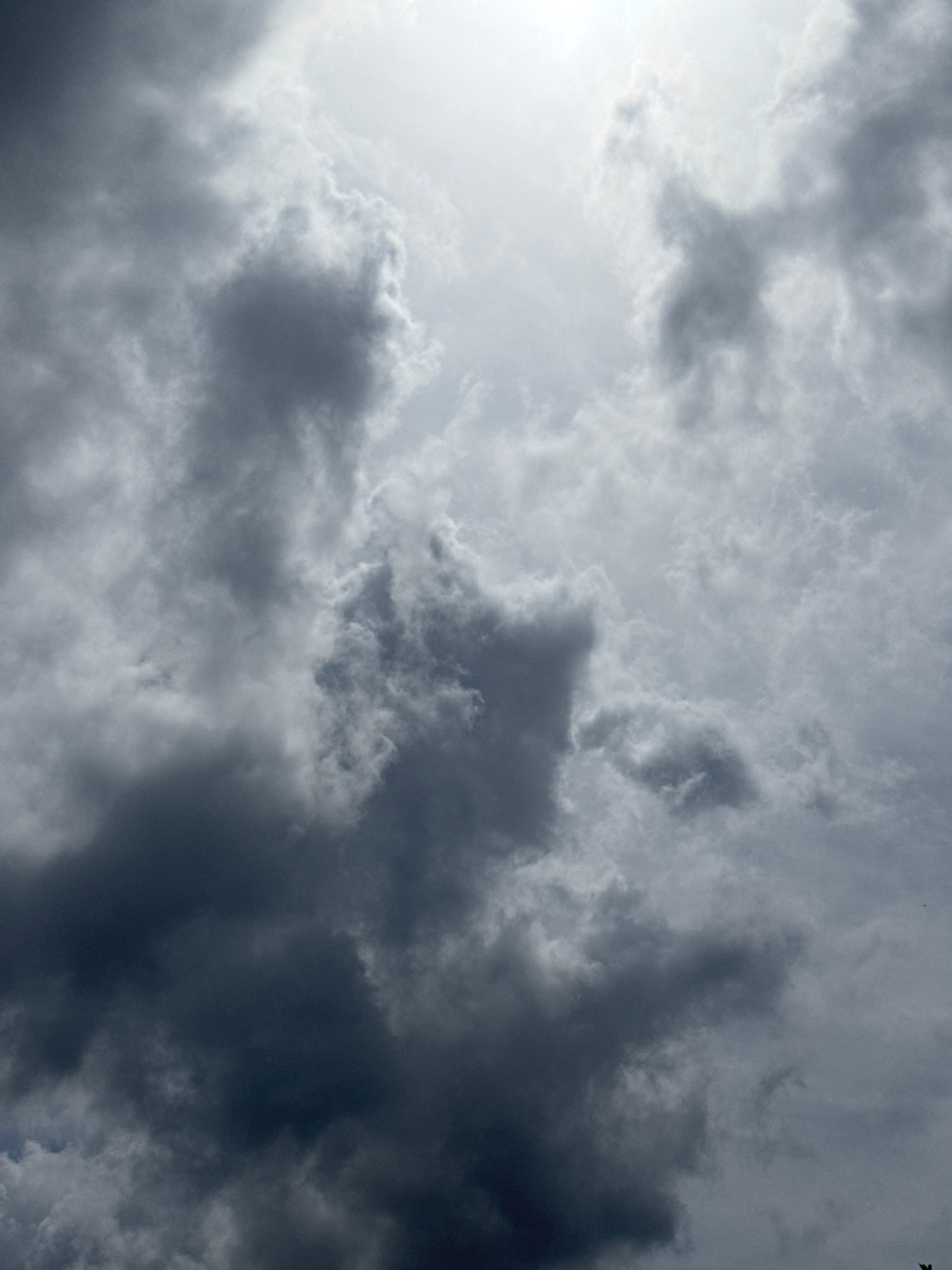 The image shows a sky filled with dramatic, dark storm clouds. The clouds are heavy and ominous, with a stark contrast between the darker, shadowed areas and the brighter, lighter areas where the sun is attempting to break through. The overall mood of the image is dramatic and foreboding, suggesting an impending storm. The location is not discernible from the image itself.