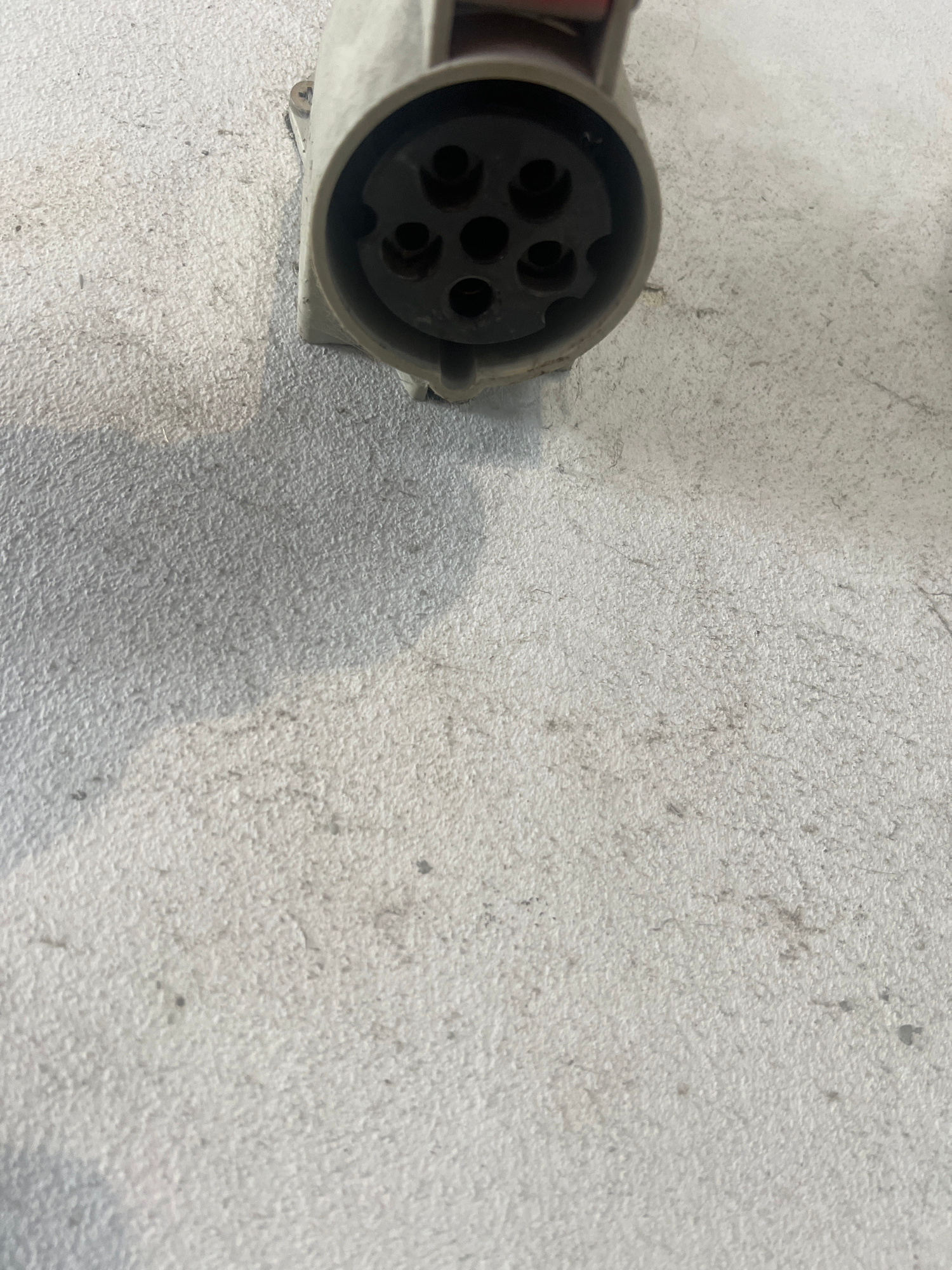 A close-up, high-angle shot shows a light-colored, round electrical connector with five circular openings. The connector is on a textured, light gray surface. The connector is located in the city of Тэльмінскі сельскі Савет, Belarus.