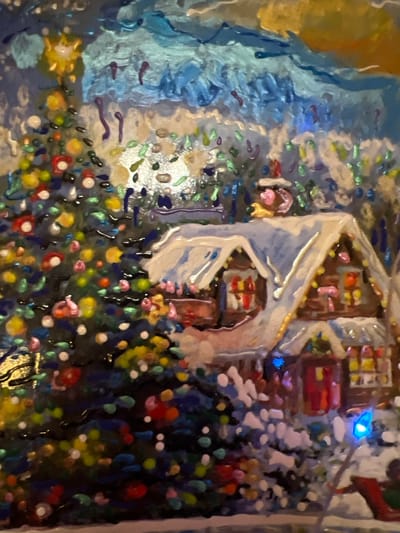 This is a close-up, textured painting of a festive winter scene. A decorated Christmas tree, adorned with colorful baubles, stands to the left of a snow-covered house. The house features illuminated windows and a chimney with smoke. The background consists of abstract blue and yellow brushstrokes suggesting a night sky or festive lights. There are no visible people or specific landmarks indicating a location in Minsk, Belarus.